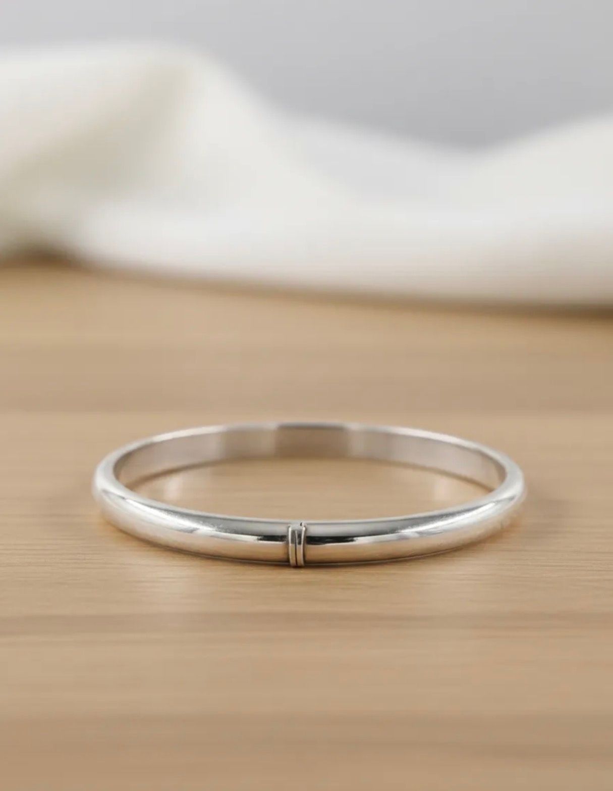 Brazalete de plata sobre una caja blanca con cinta de satén y flores de orquídea blanca.