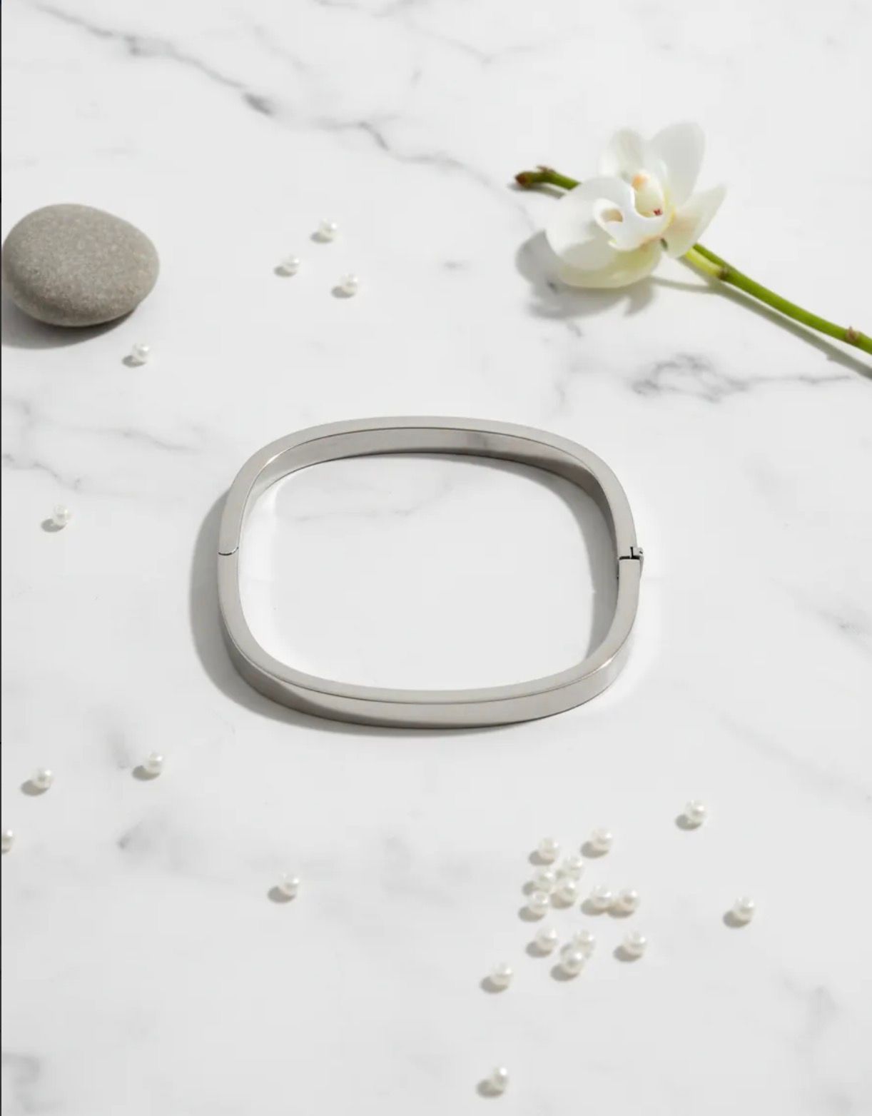 Anillo ovalado de plata sobre una superficie de tela color crema con suaves sombras y pequeñas piedras cerca.