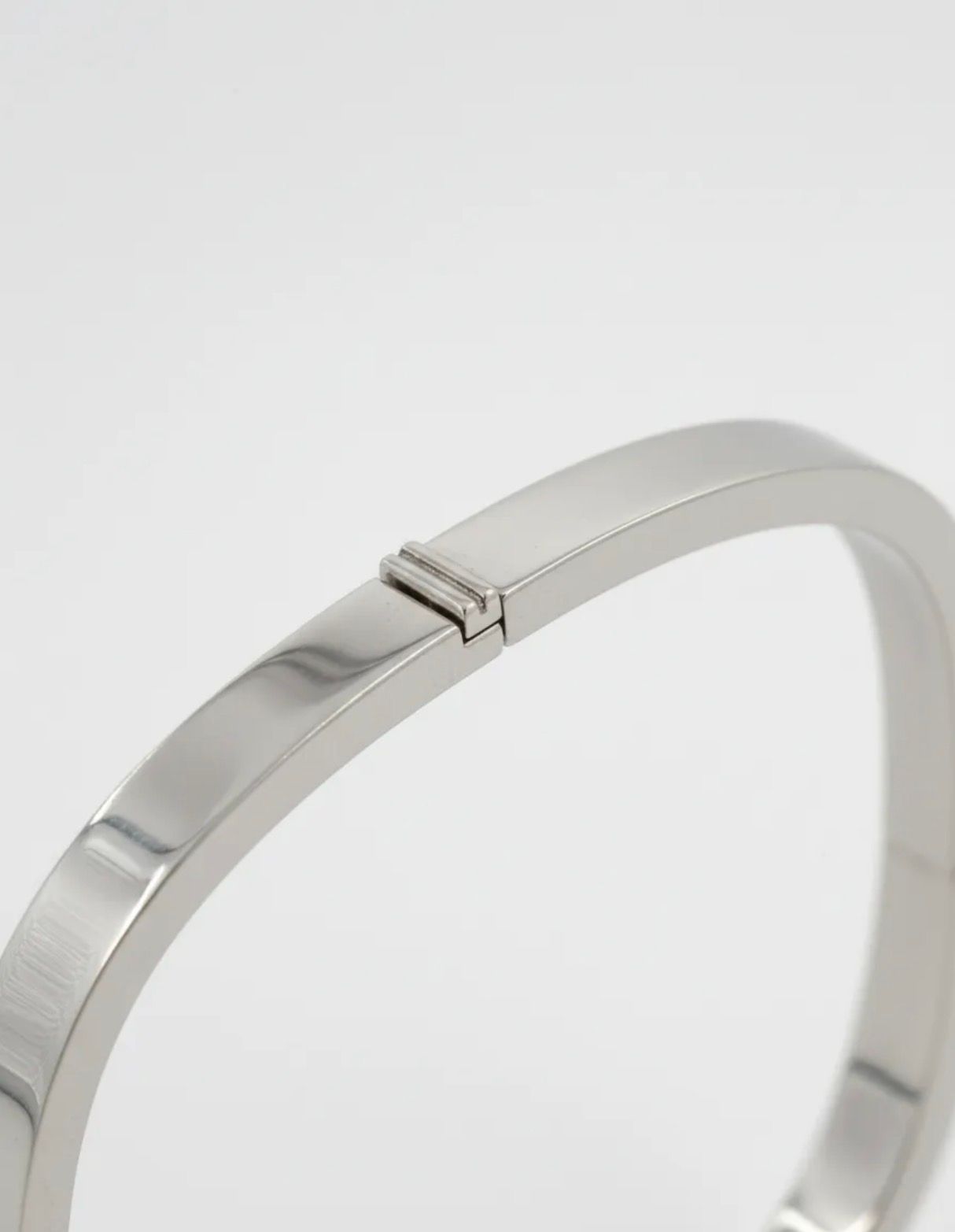 Pulsera cuadrada de plata sobre mármol blanco junto a hojas verdes y una pequeña piedra.