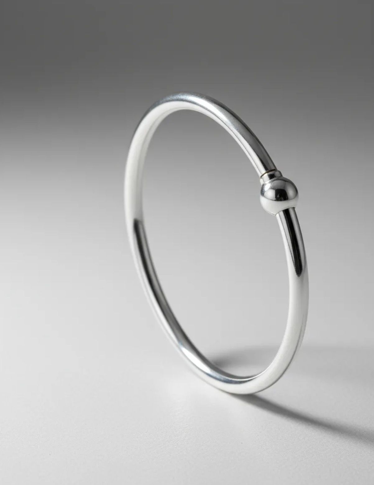 Pulsera de plata sobre una superficie de mármol con tela de seda, una piedra blanca y una flor de orquídea.