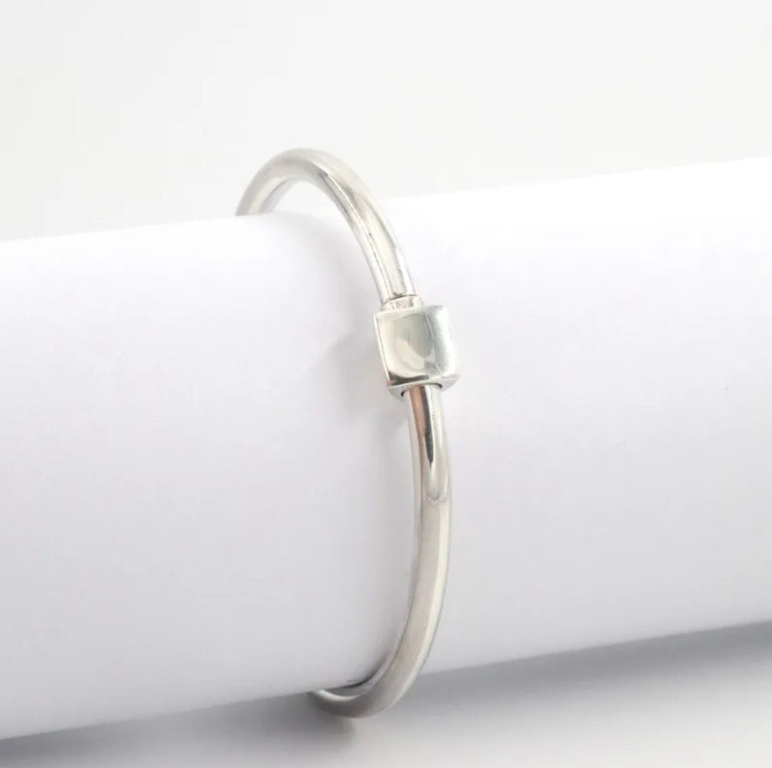 Pulsera de plata con una pequeña cuenta, sobre una superficie de mármol con hojas de eucalipto cerca.
