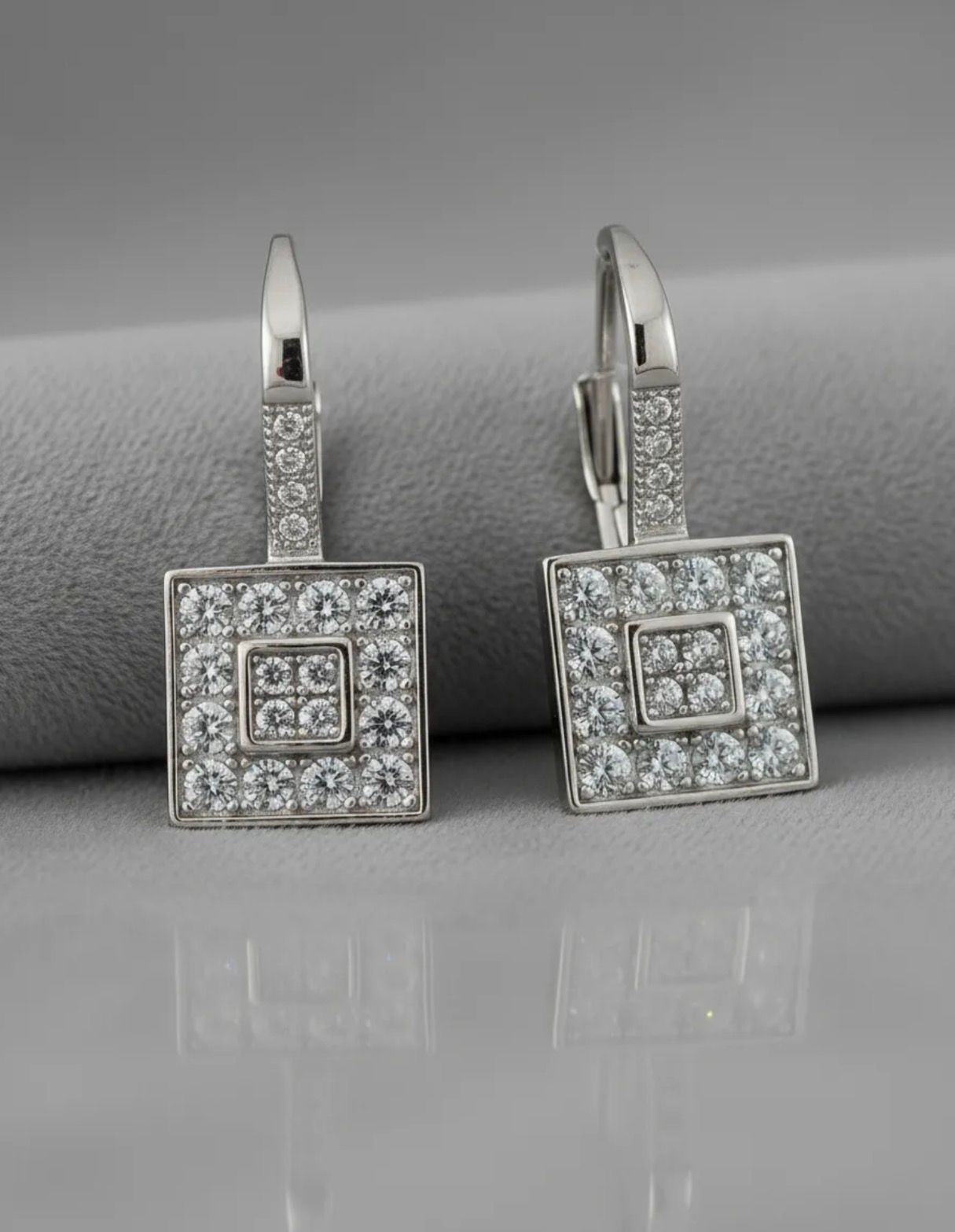 Par de pendientes colgantes cuadrados con incrustaciones de diamantes sobre un fondo de tela clara.
