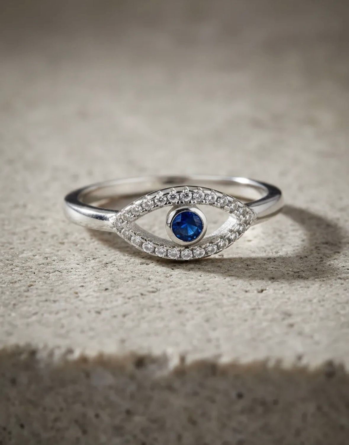 Anillo de plata con una piedra preciosa azul y pequeñas piedras transparentes sobre una superficie de mármol blanco.