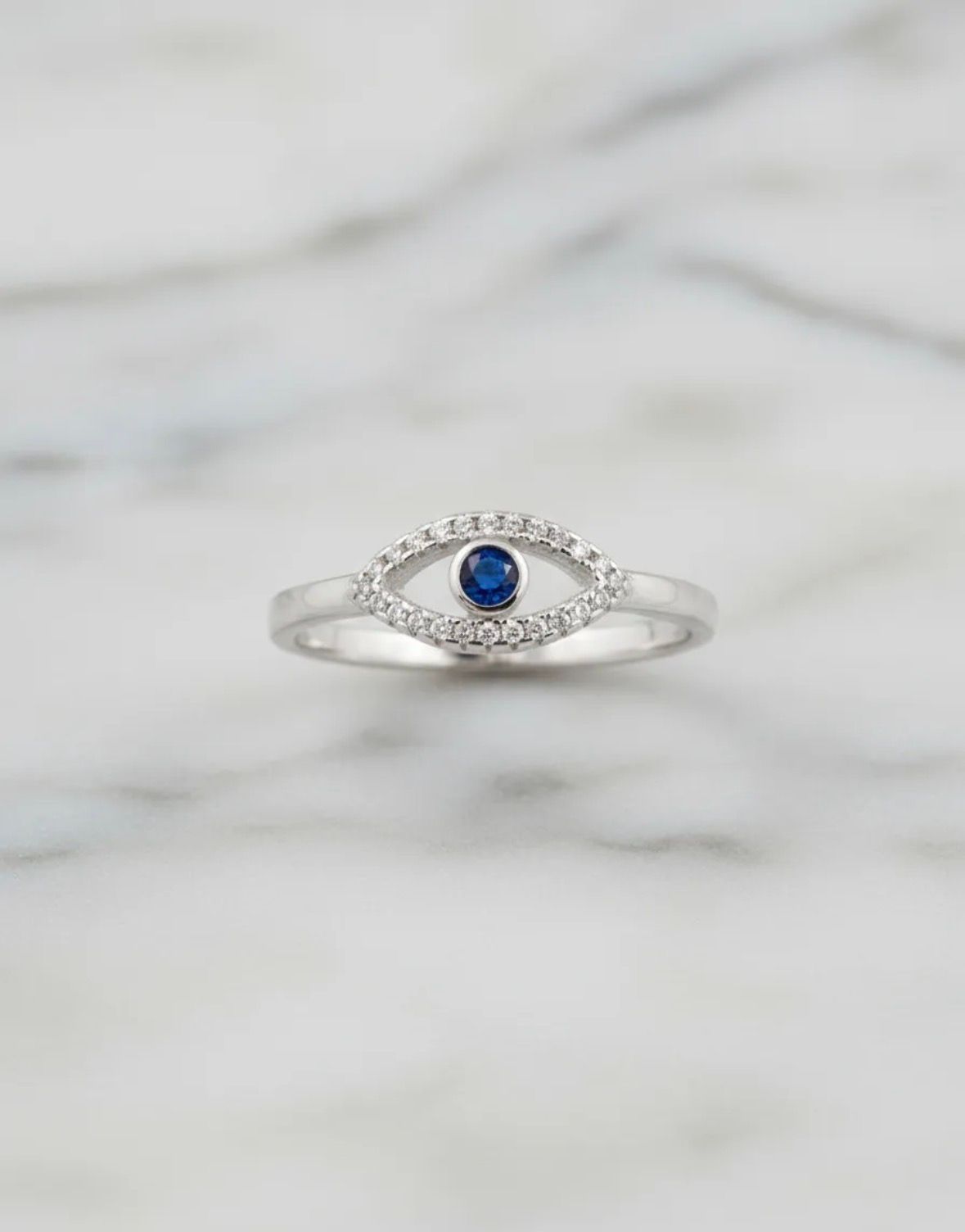 Anillo de plata con una piedra preciosa azul y pequeñas piedras transparentes sobre una superficie de mármol blanco.