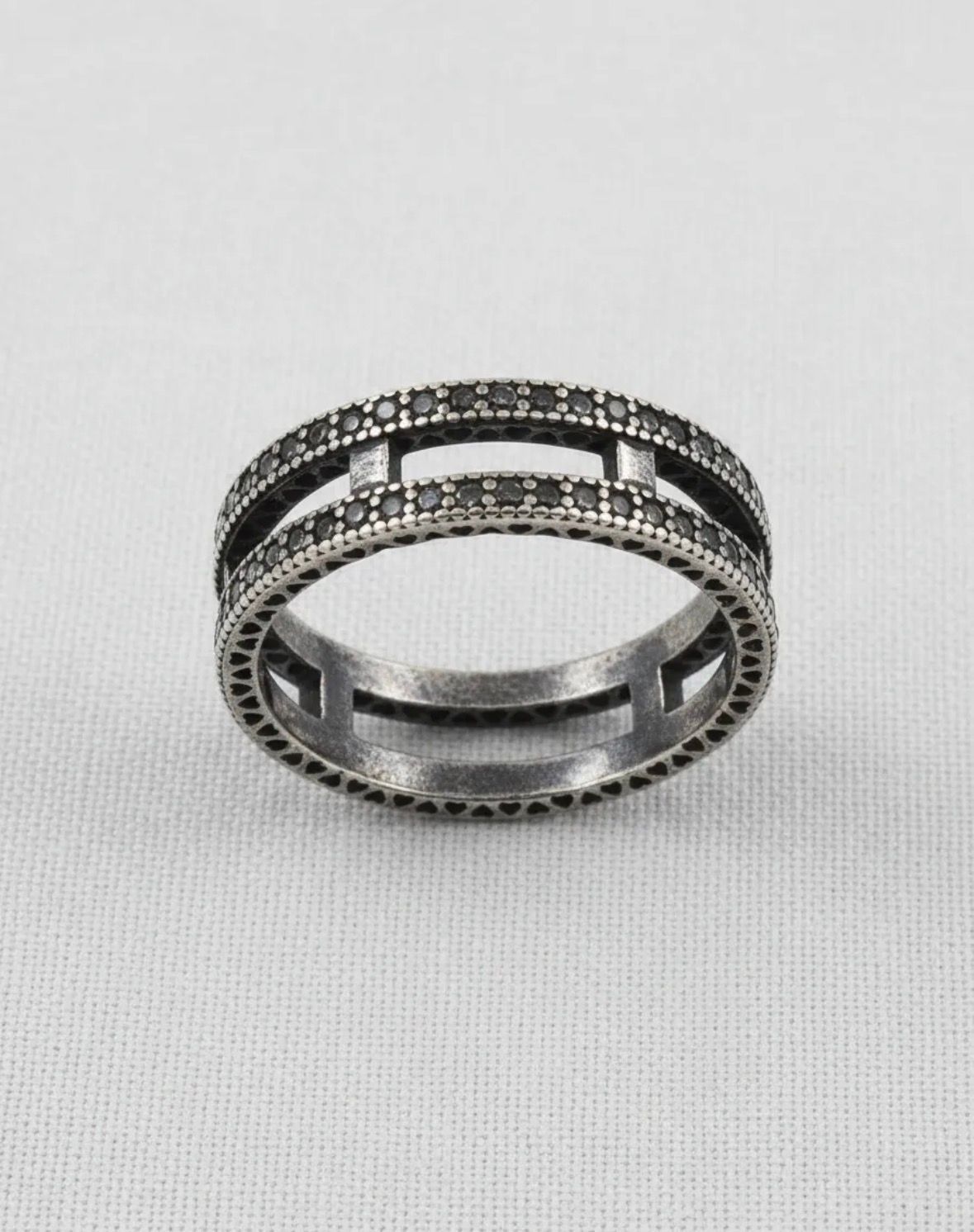 Dos anillos de plata apilados, cada uno con hileras de pequeñas piedras oscuras.