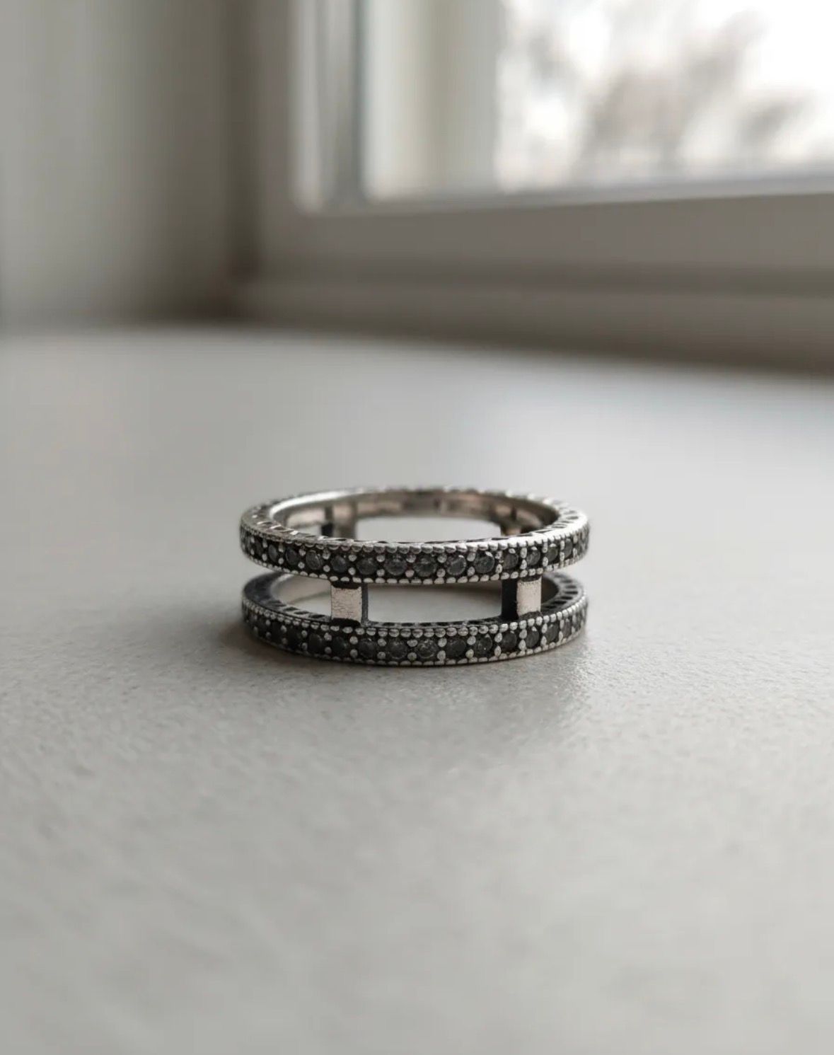 Dos anillos de plata apilados, cada uno con hileras de pequeñas piedras oscuras.