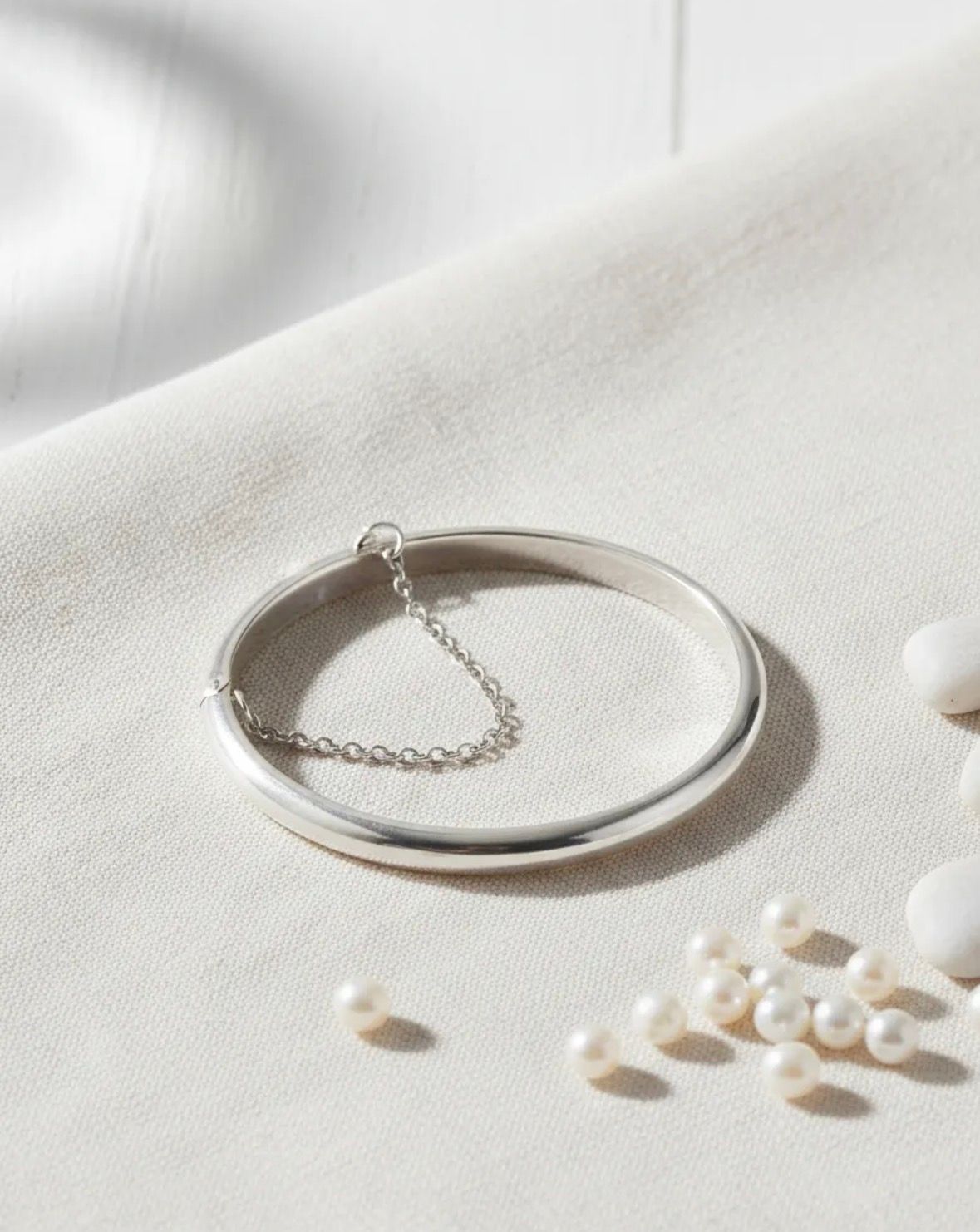 Anillo abierto de plata con una sombra de cadena colgante sobre un fondo claro.