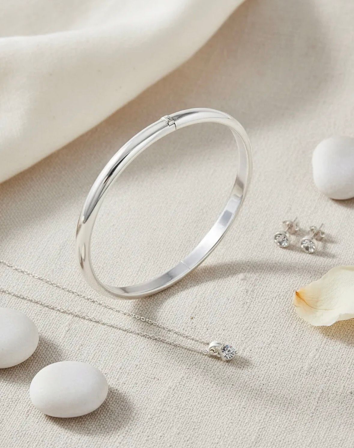 Pulsera de plata sobre tela beige con pequeñas piedras blancas y flores secas.