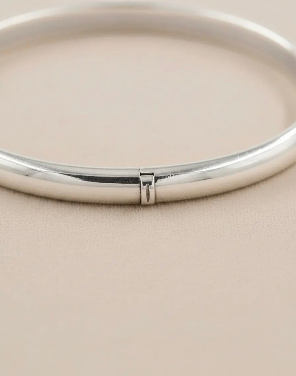 Anillo redondo de metal y cinta beige sobre una superficie de mármol blanco con una piedra negra y flores secas.