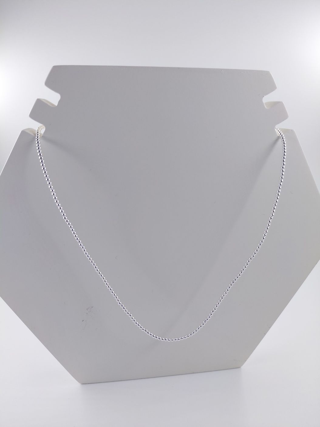 Busto blanco para exhibición de joyas con un collar de cadena de plata sobre fondo gris claro.