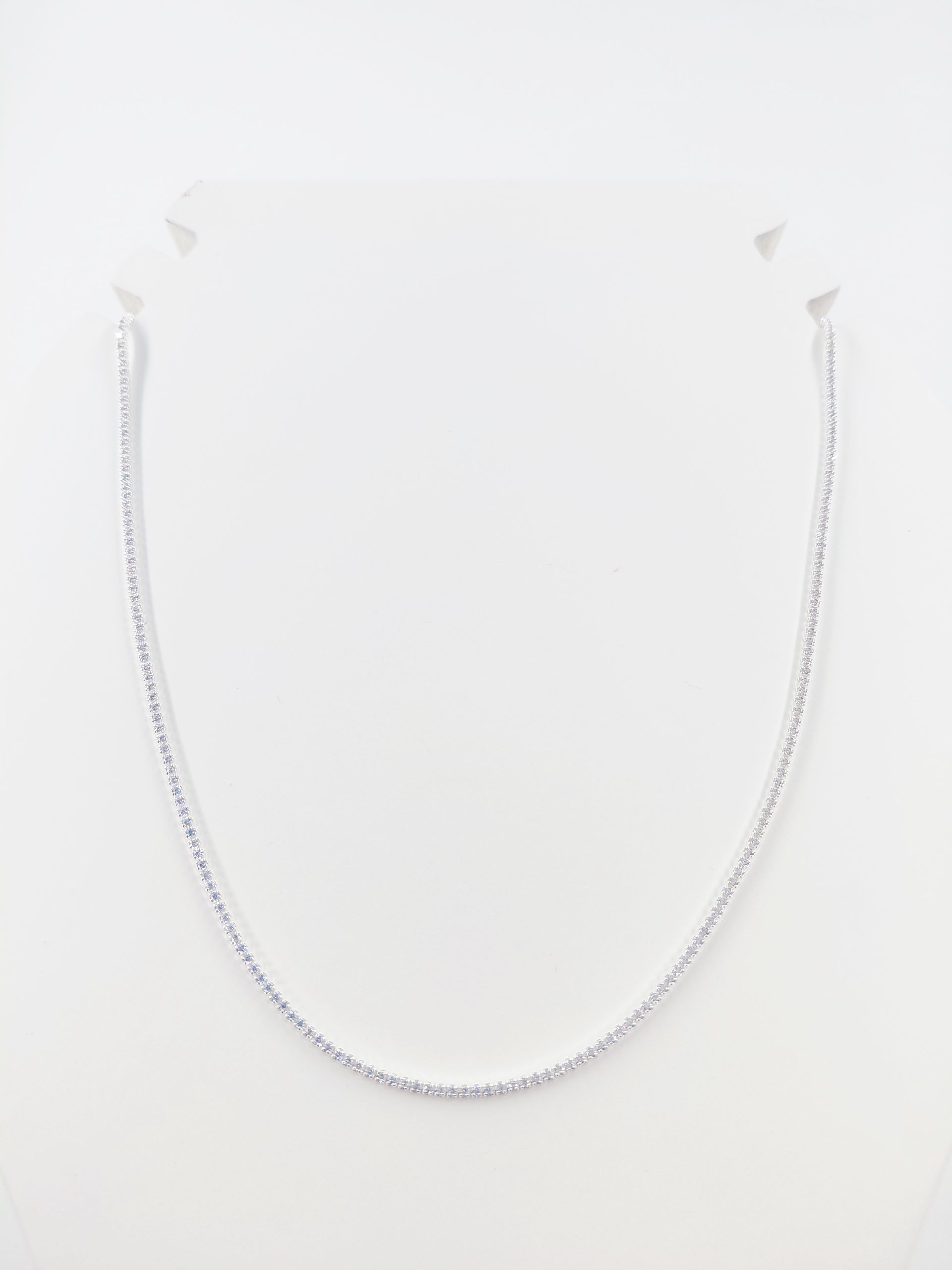 Collar de delicada cadena de plata sobre un soporte blanco.