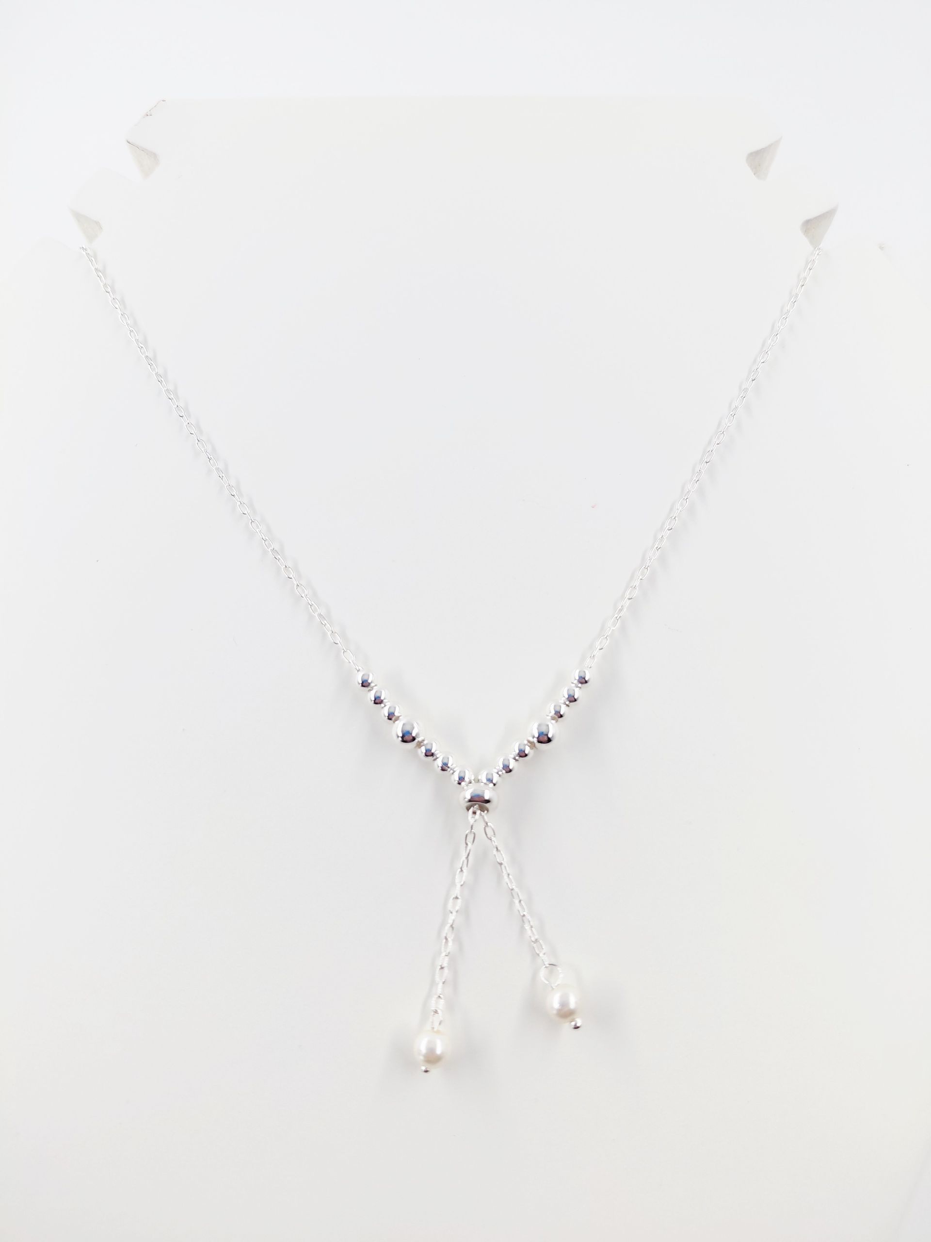 Collar de plata con un colgante en forma de Y y colgantes en forma de lágrima sobre un fondo blanco.