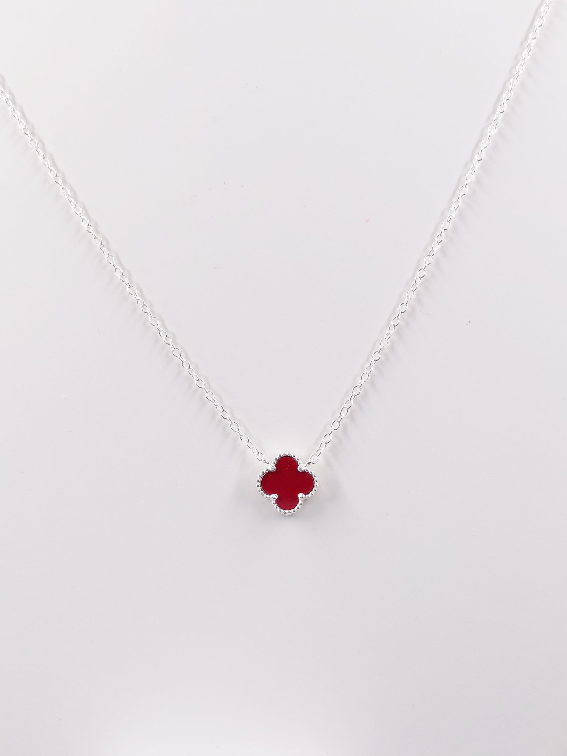 Collar de plata con un pequeño colgante de piedra preciosa roja sobre un fondo claro.