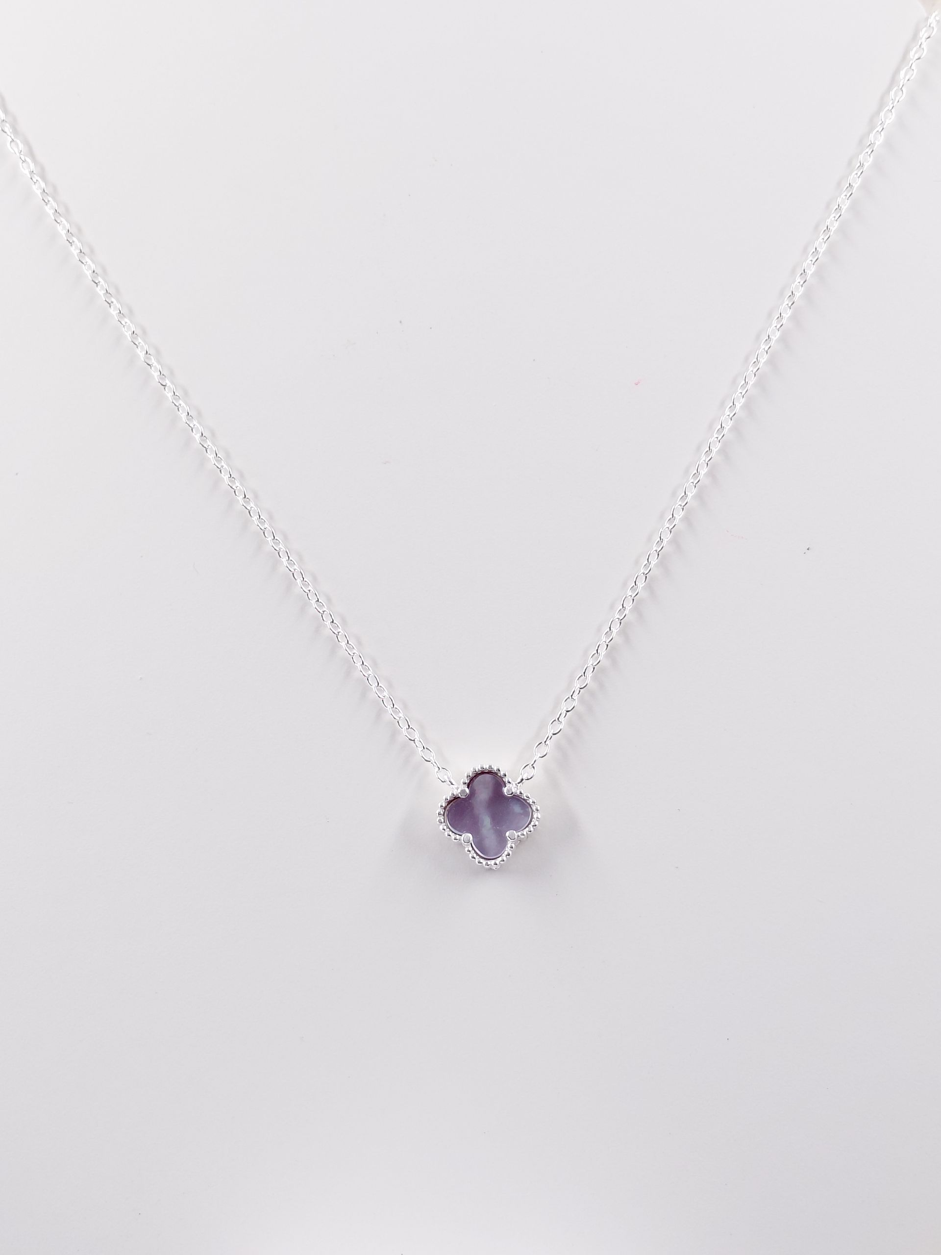 Collar de plata con un pequeño colgante de piedra preciosa morada sobre fondo blanco.
