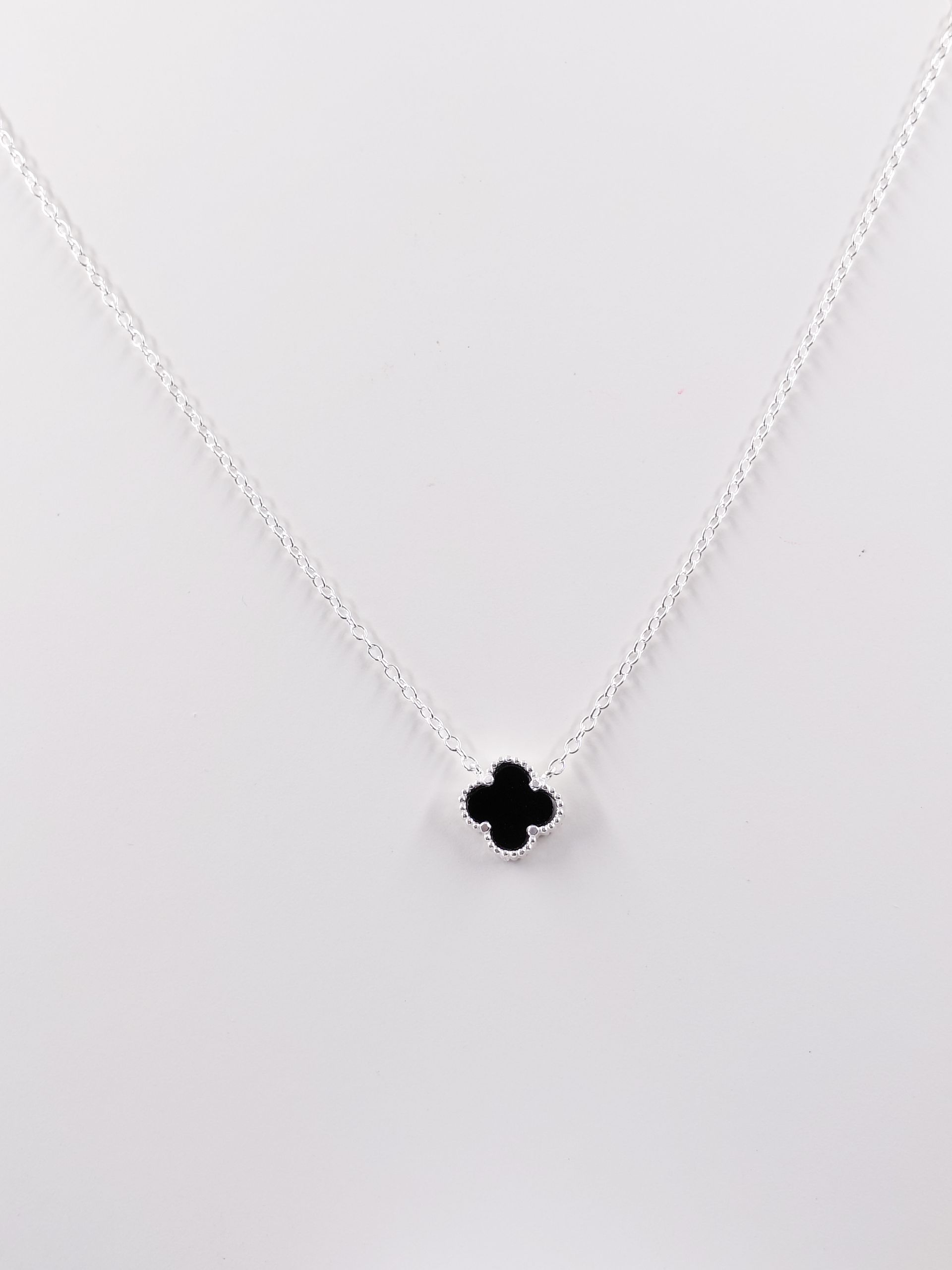 Collar de plata con un pequeño colgante de trébol de cuatro hojas negro sobre fondo blanco.