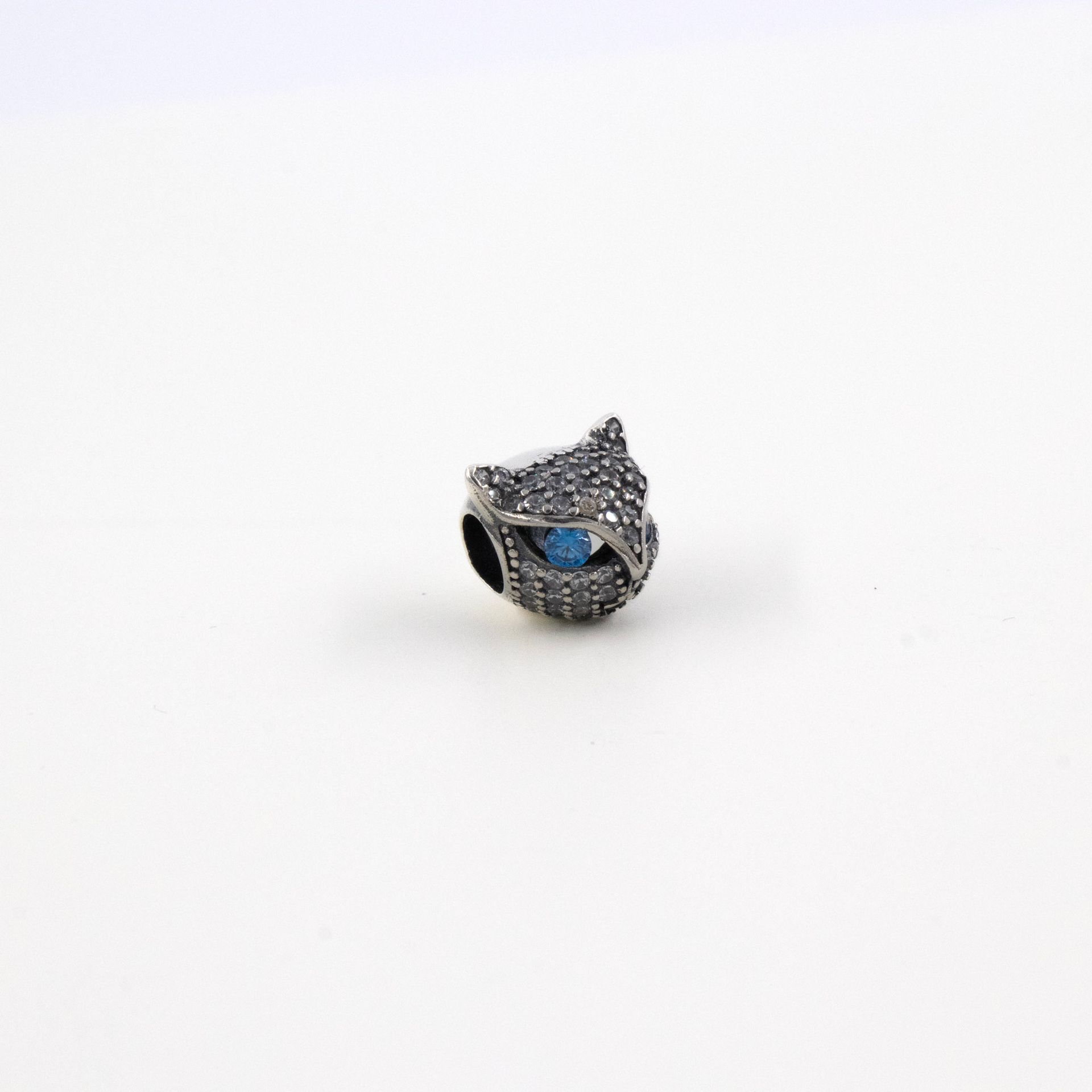 Collar de plata con detalles de cuentas azules y transparentes, con un colgante en forma de cabeza de gato sobre fondo gris.