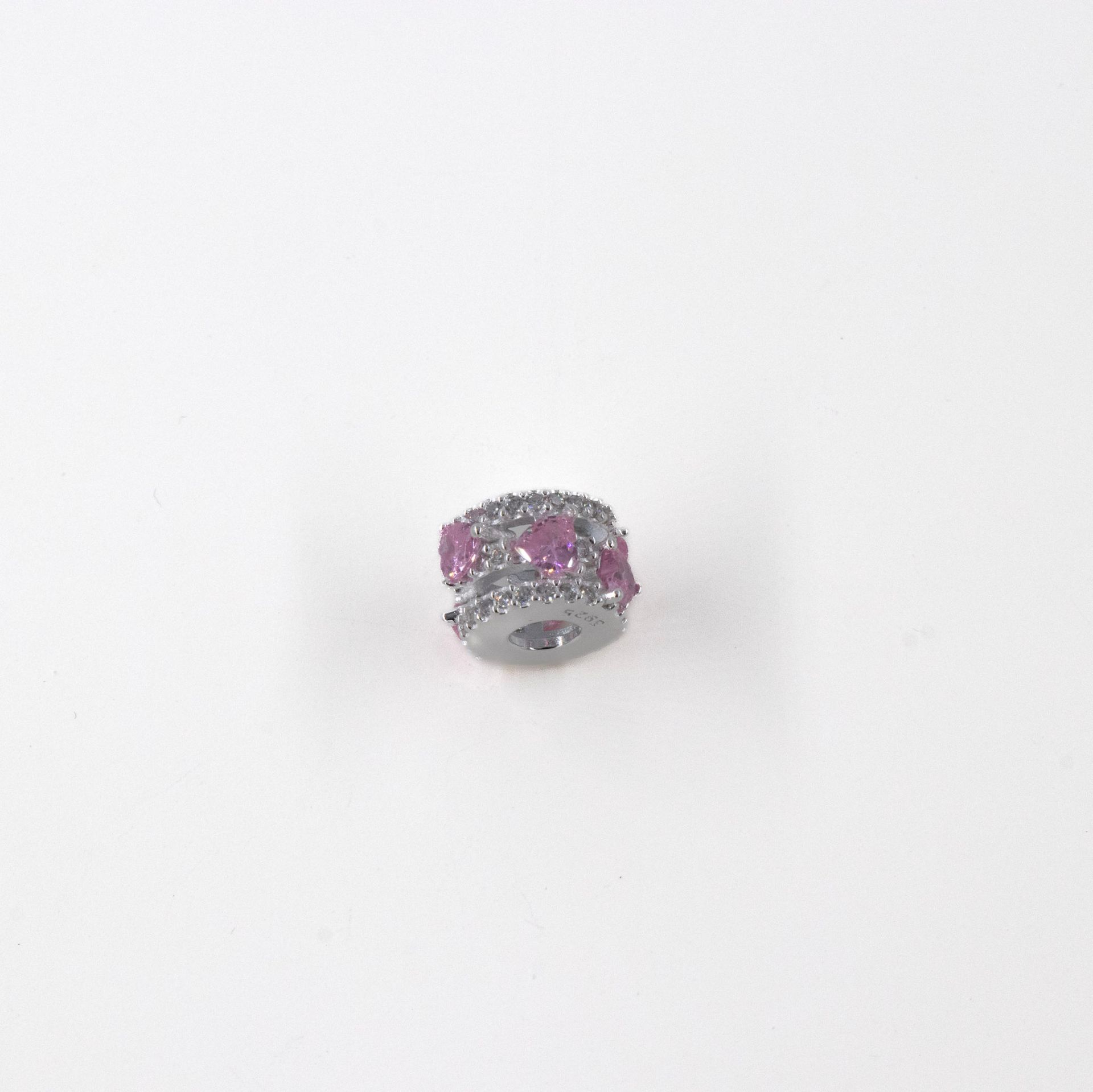 Anillo pequeño de plata con piedras preciosas rosas sobre fondo blanco.