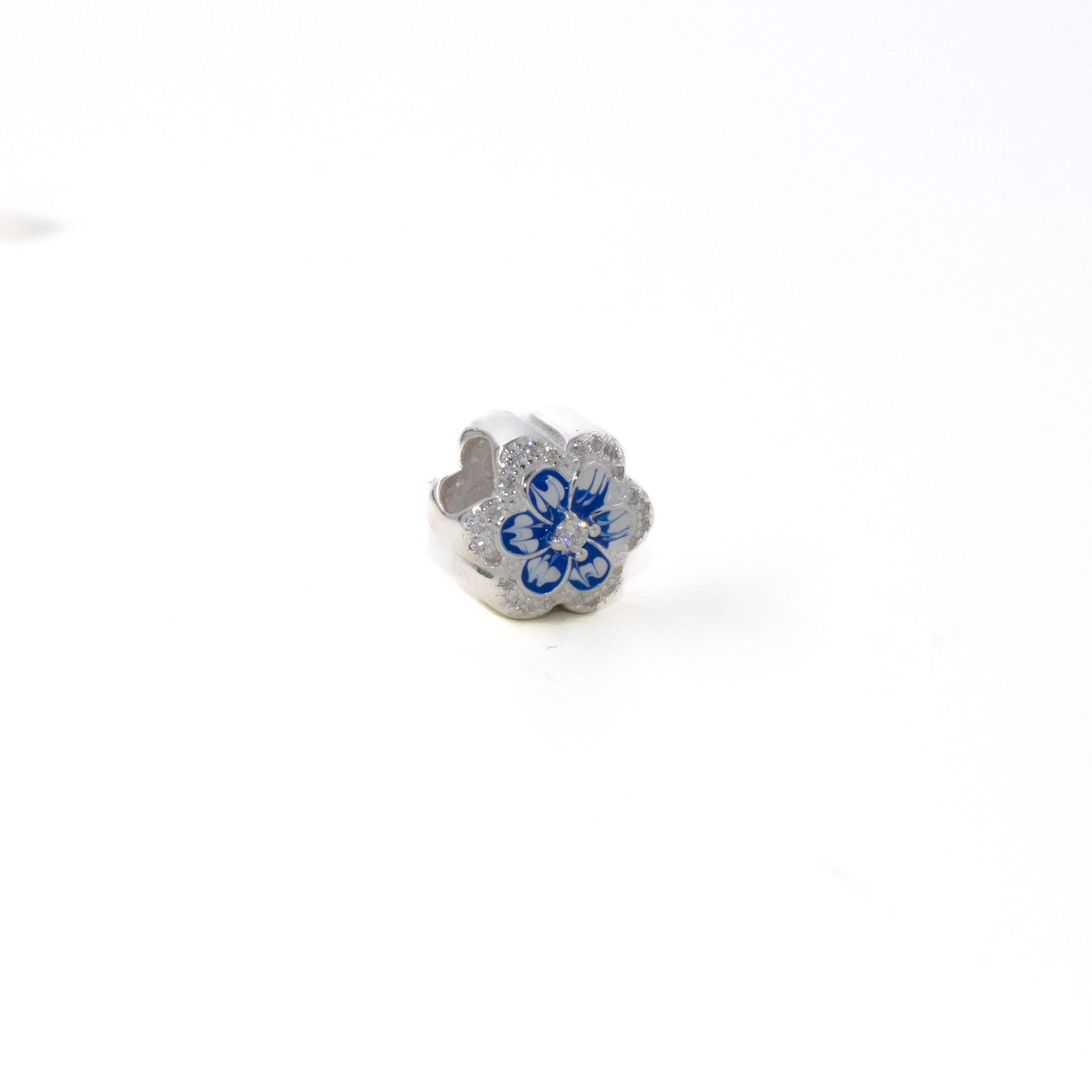 Pequeña cuenta plateada en forma de flor con centro azul sobre fondo blanco.