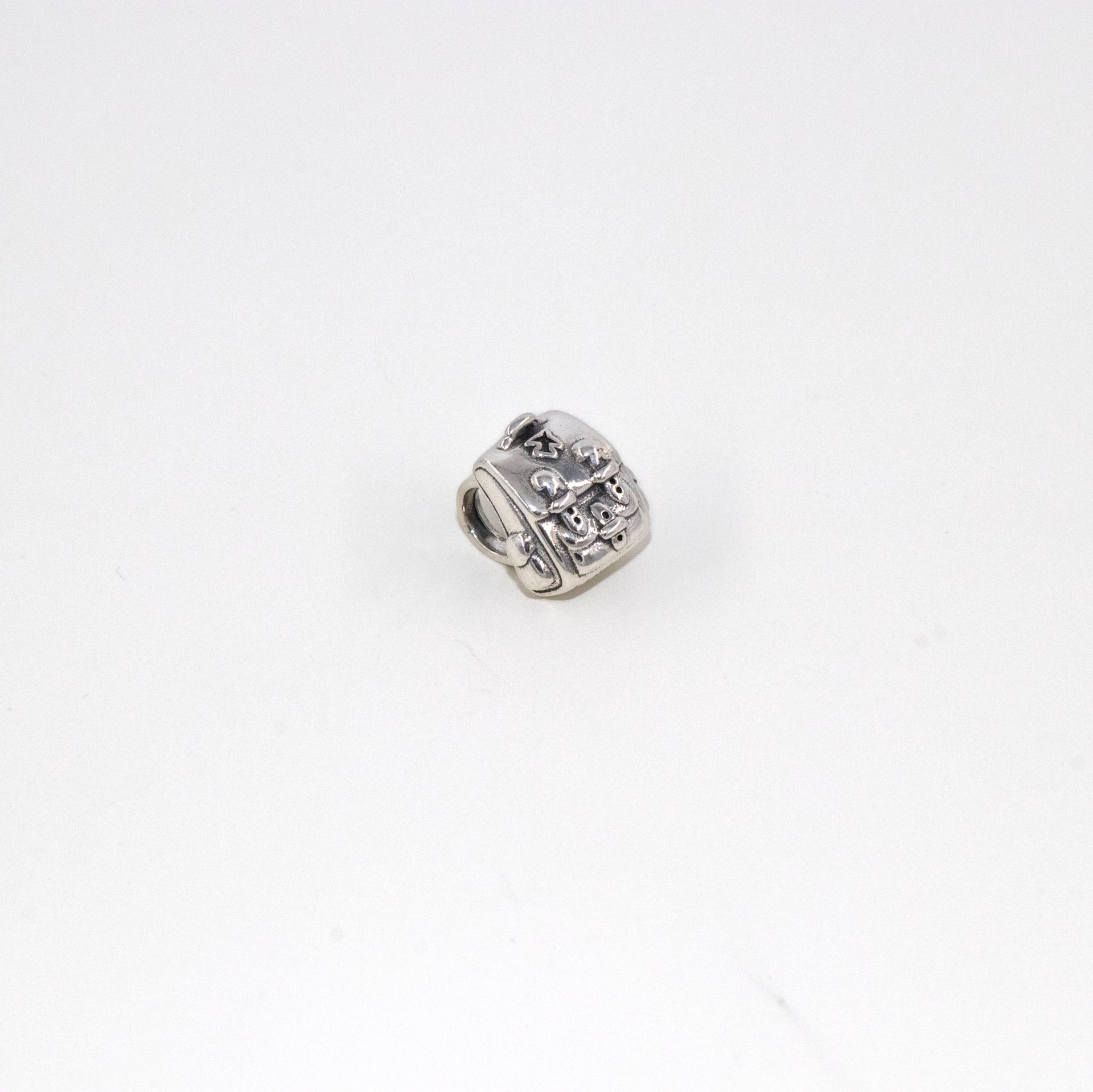 Pequeño dije de plata con un diseño floral oscuro sobre fondo blanco.