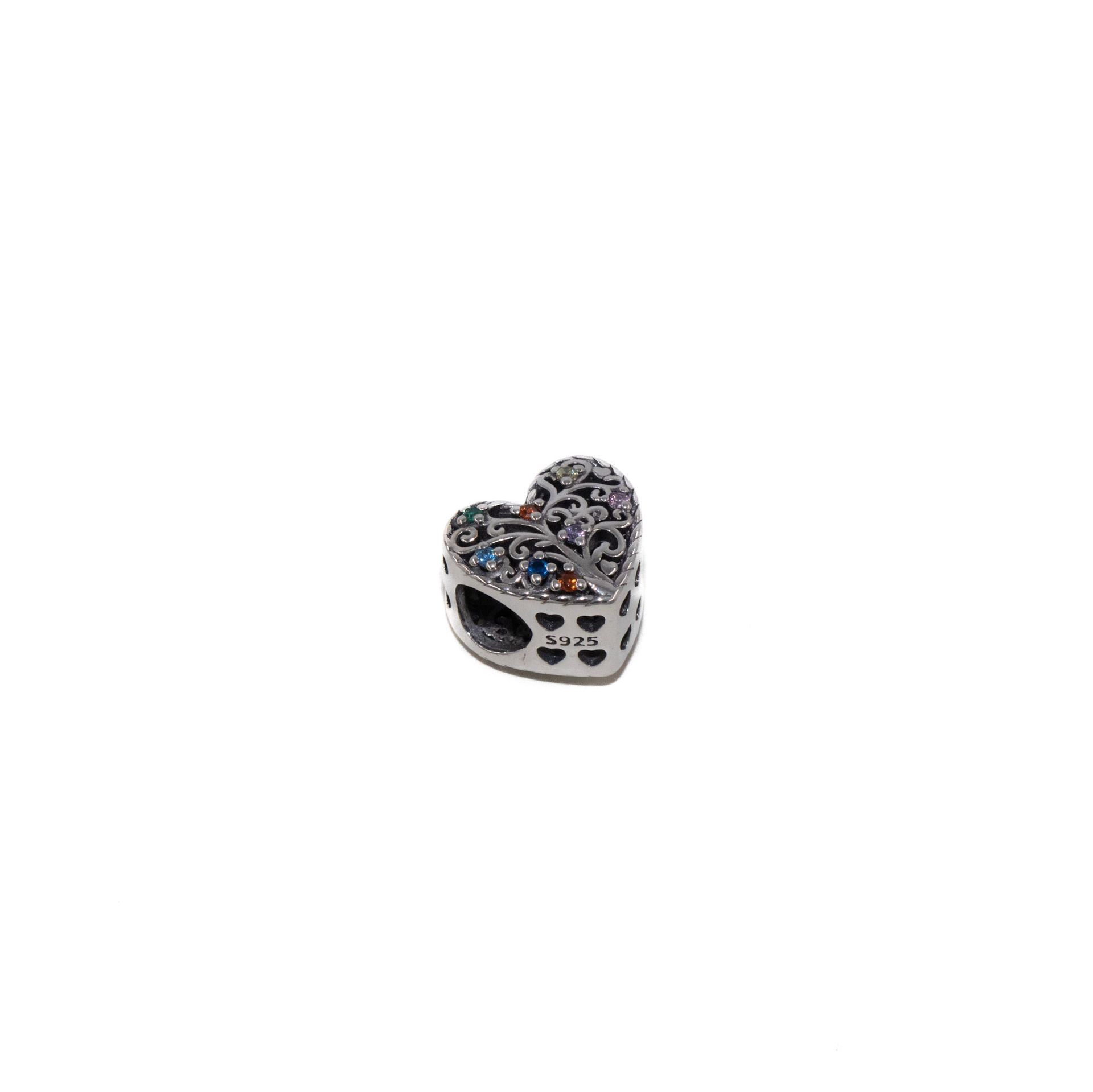 Pequeño dije plateado en forma de corazón con piedras negras y transparentes sobre fondo blanco.