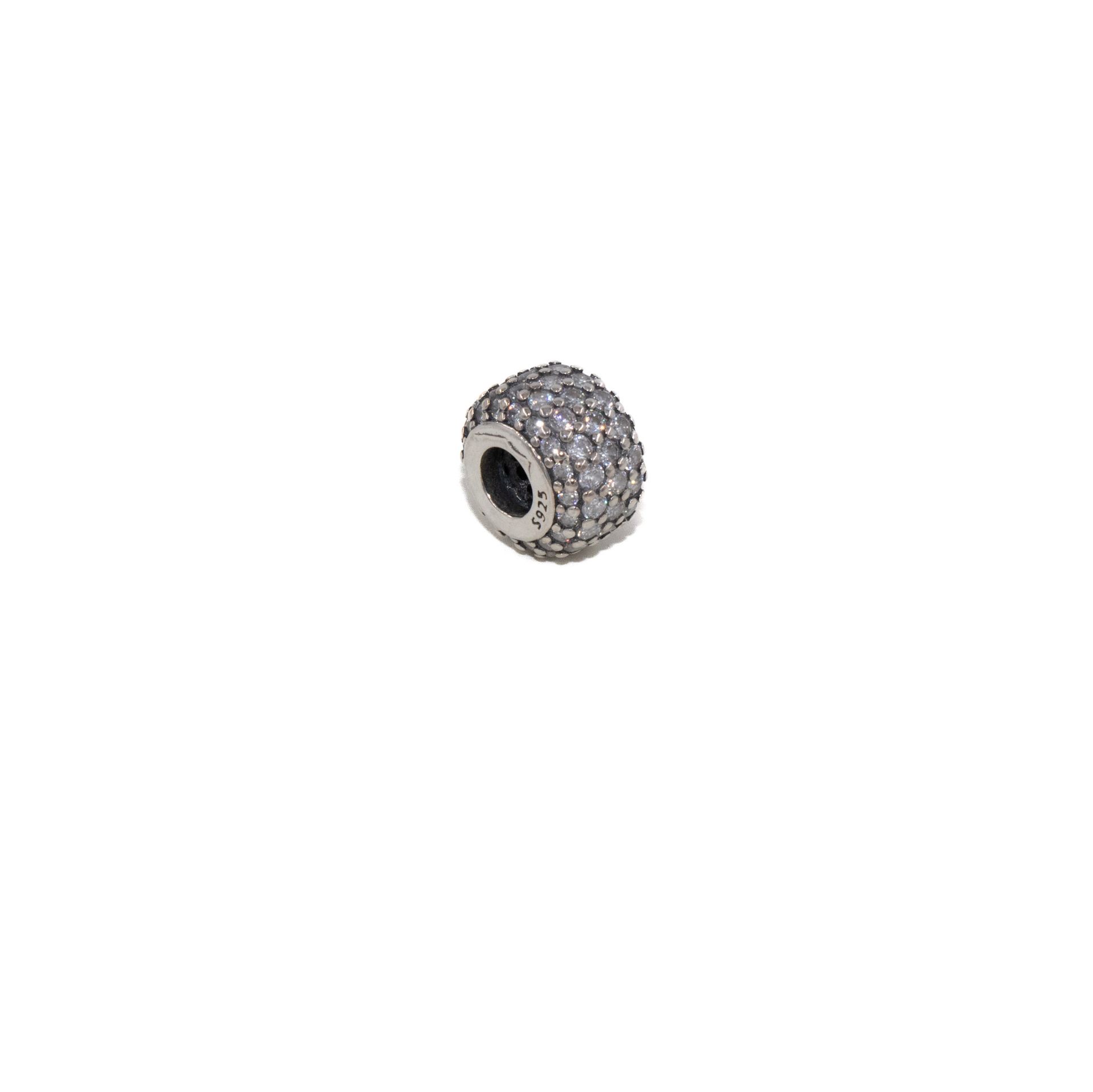 Pequeña cuenta de plata u objeto con forma de rueda sobre un fondo blanco.