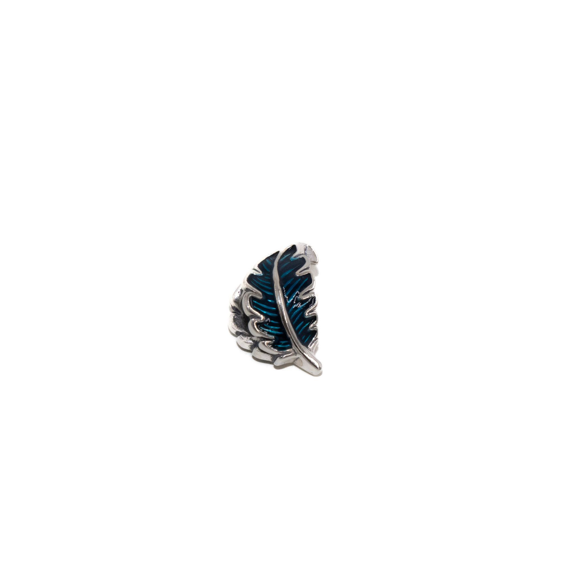 Pequeño broche plateado y azul marino con forma de pluma sobre fondo blanco.