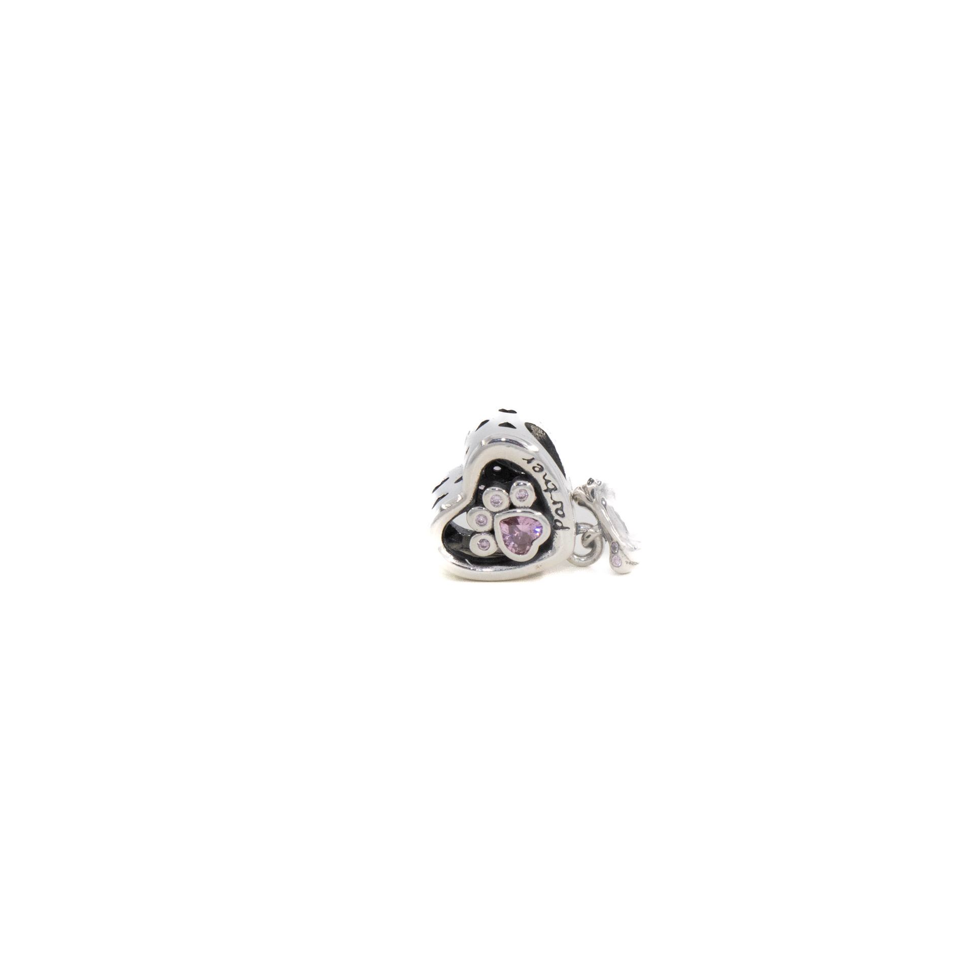 Pequeña pieza de joyería plateada con forma de flor y centro rosa sobre fondo blanco.