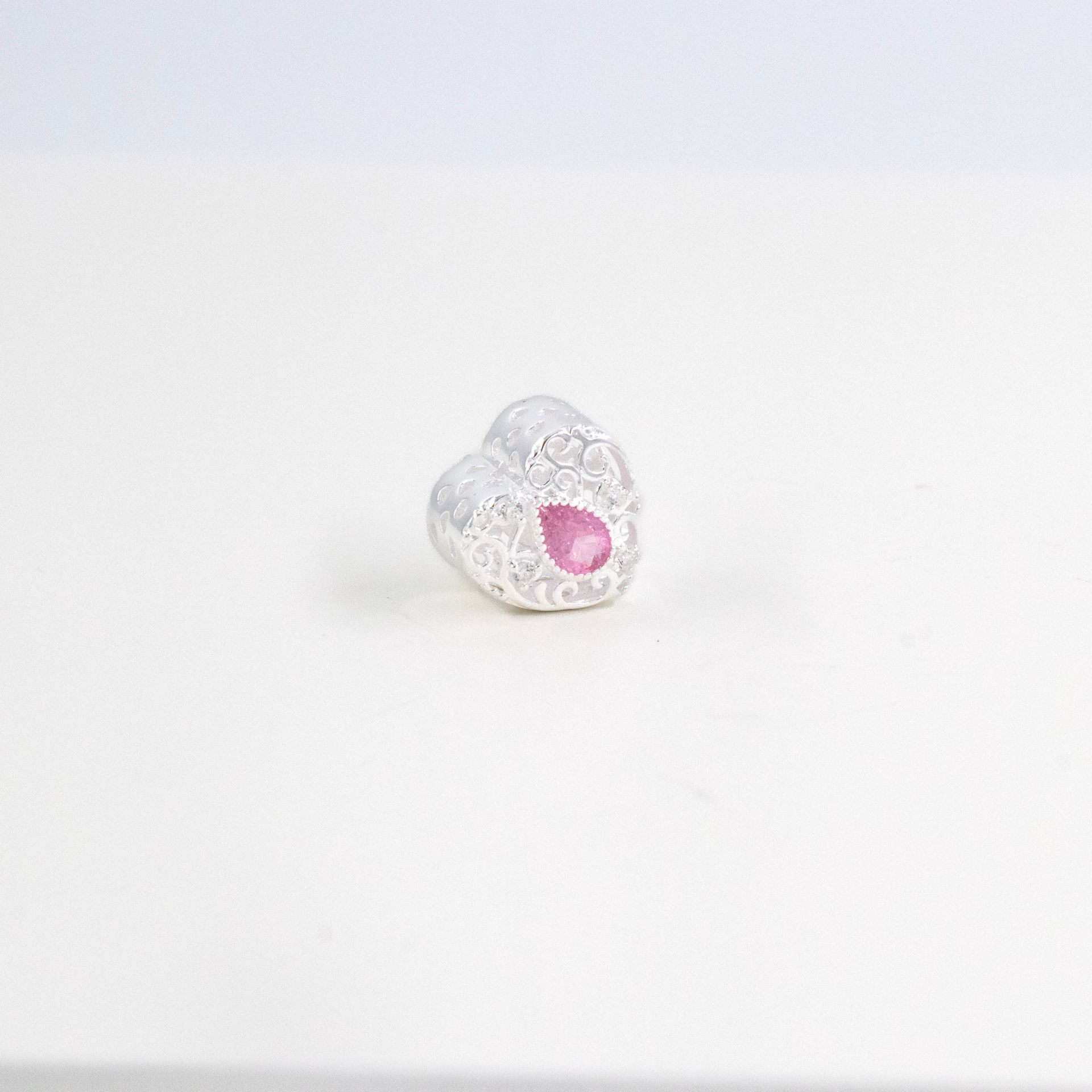 Pequeño dije blanco translúcido en forma de corazón con centro rosa sobre fondo blanco.