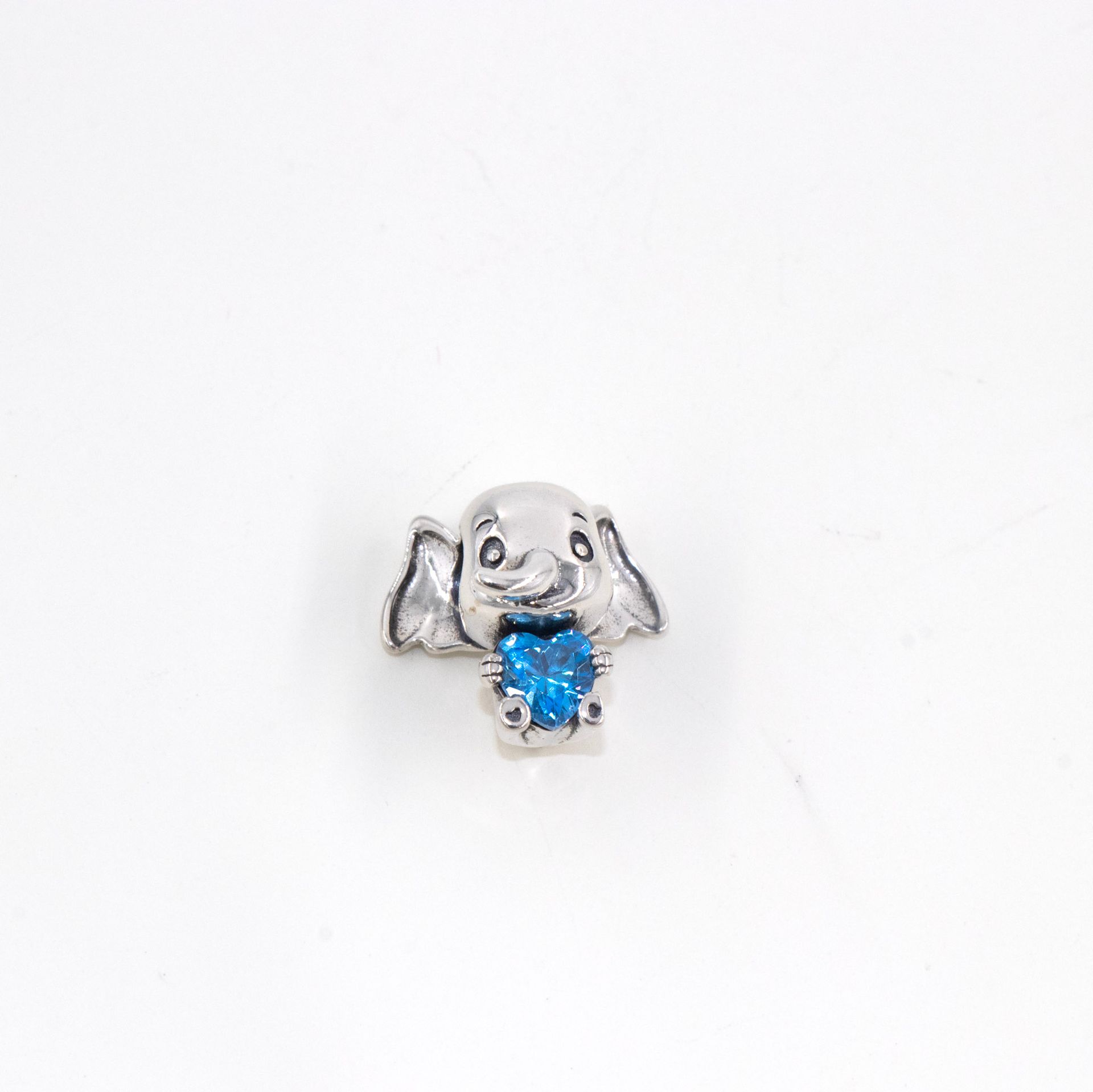 Colgante de elefante plateado con una piedra preciosa azul sobre fondo blanco