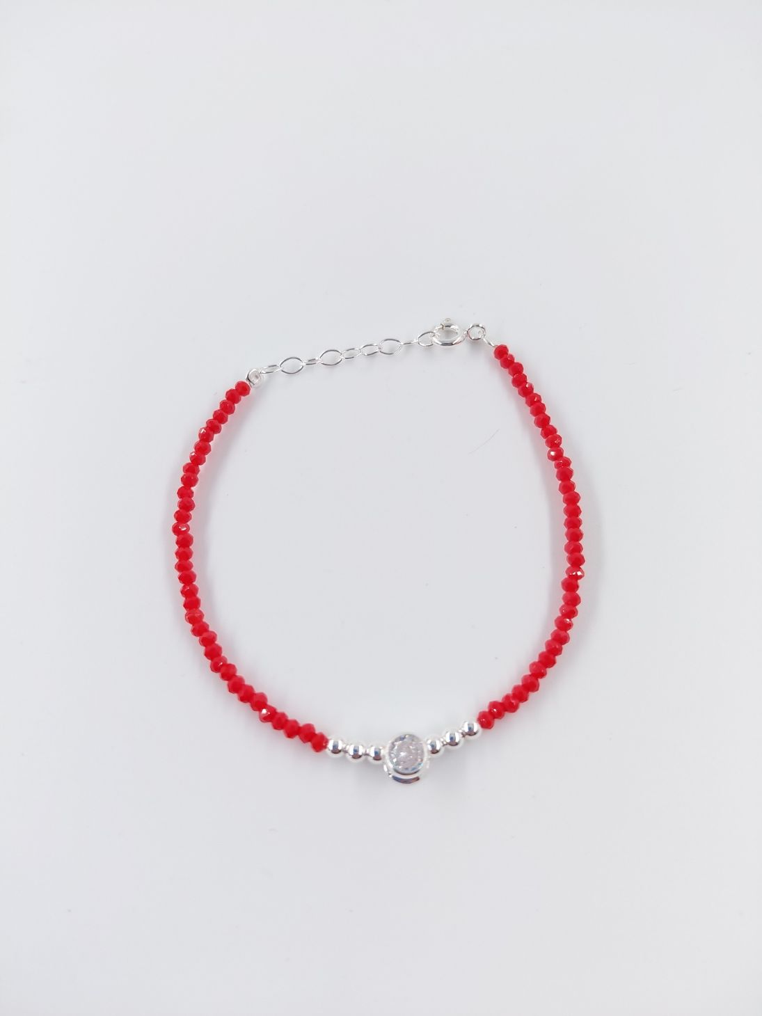 Pulsera de cuentas rojas con cierres de plata y un pequeño dije central sobre fondo blanco.
