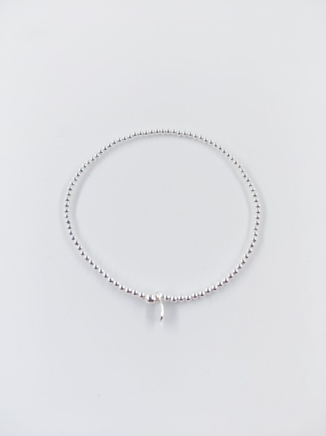 Pulsera de cuentas de plata con un pequeño dije colgante sobre fondo blanco.