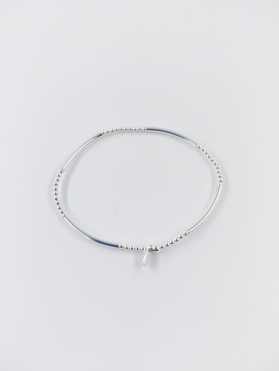 Pulsera de cuentas de plata con un pequeño dije colgante sobre fondo blanco.