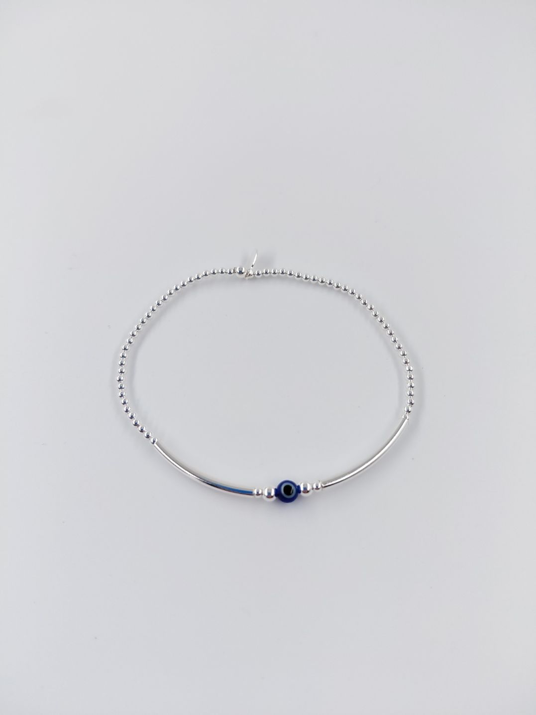 Pulsera de plata con cuentas y una pequeña cuenta azul sobre fondo blanco.