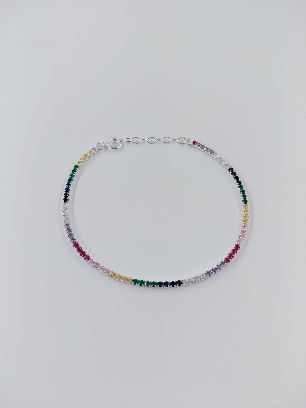 Pulsera fina de cuentas de colores del arcoíris sobre un fondo gris claro.