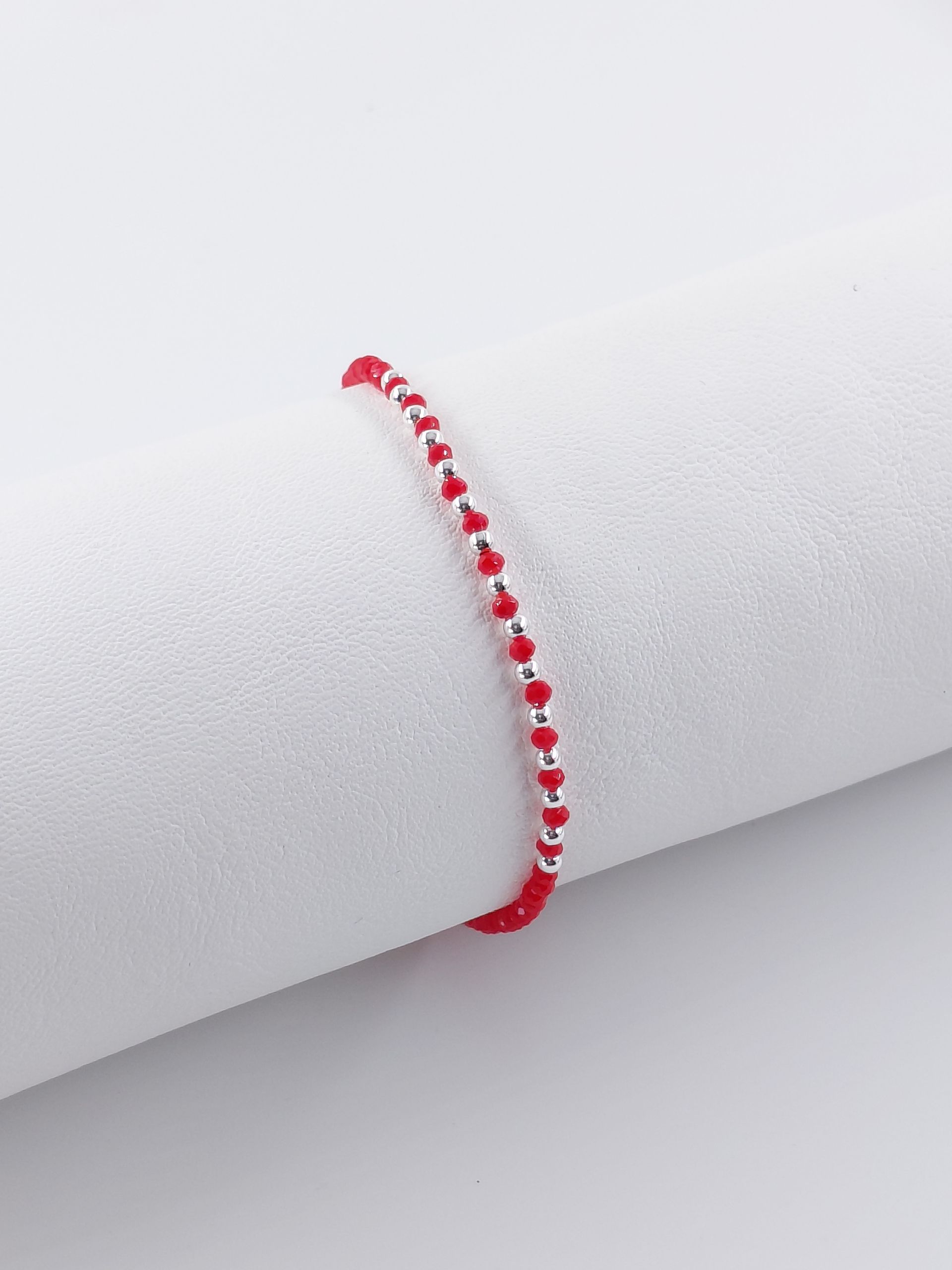 Pulsera de cuentas rojas y blancas con cierre plateado sobre fondo gris claro.