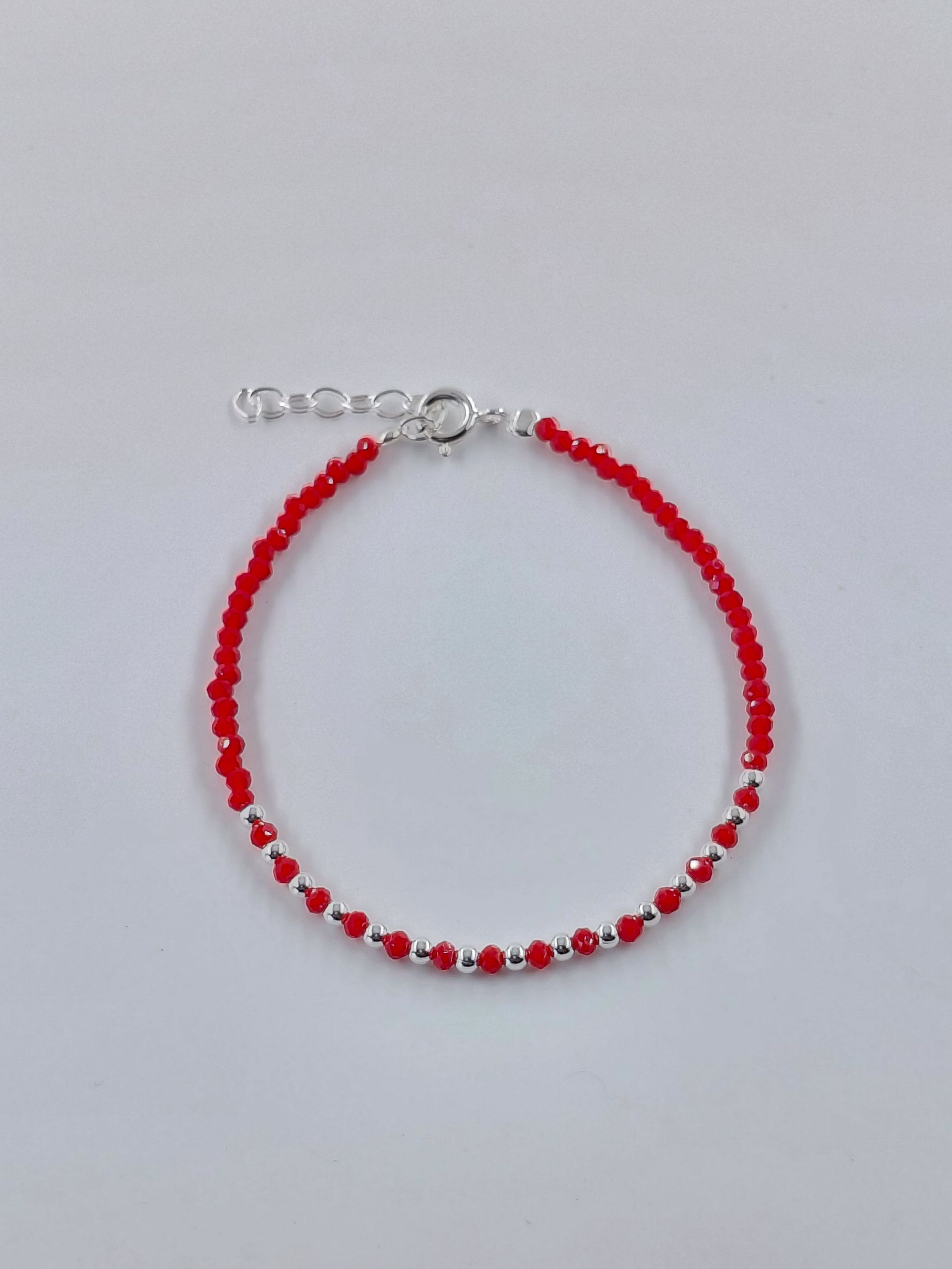 Pulsera de cuentas rojas y blancas con cierre plateado sobre fondo gris claro.
