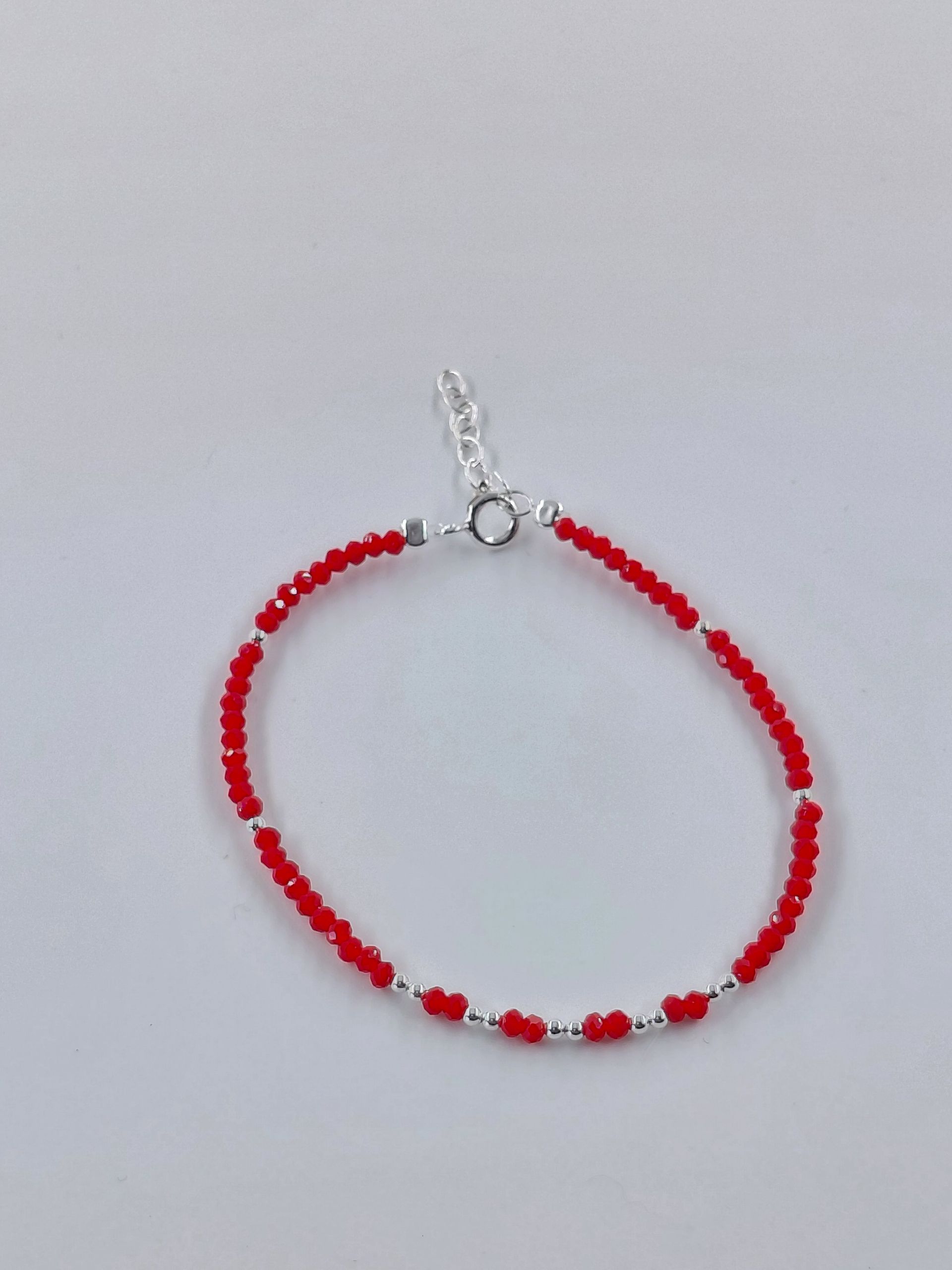 Pulsera de cuentas rojas con cierre plateado sobre fondo gris claro