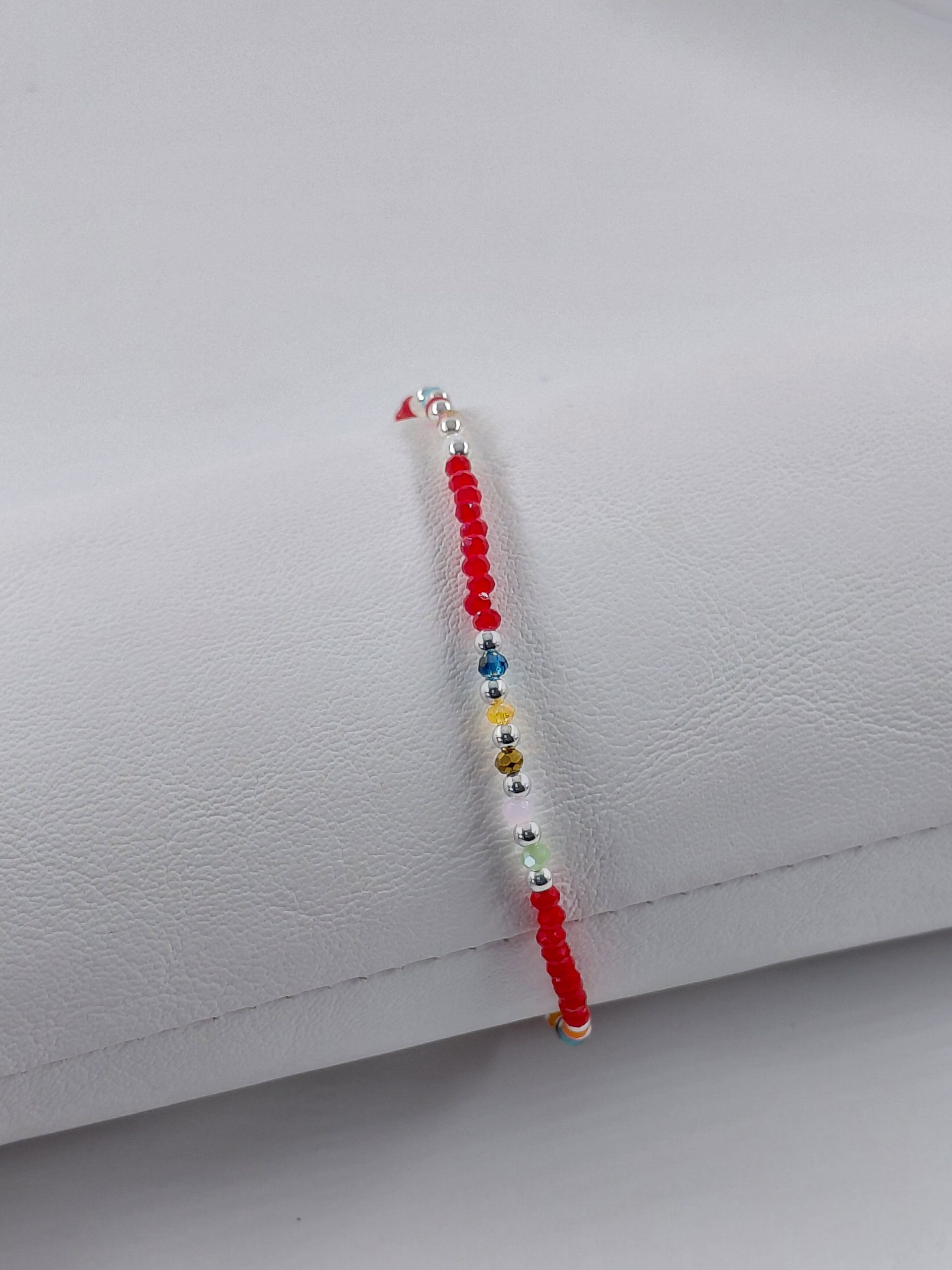 Pulsera colorida con cuentas rojas y multicolores sobre un fondo blanco.