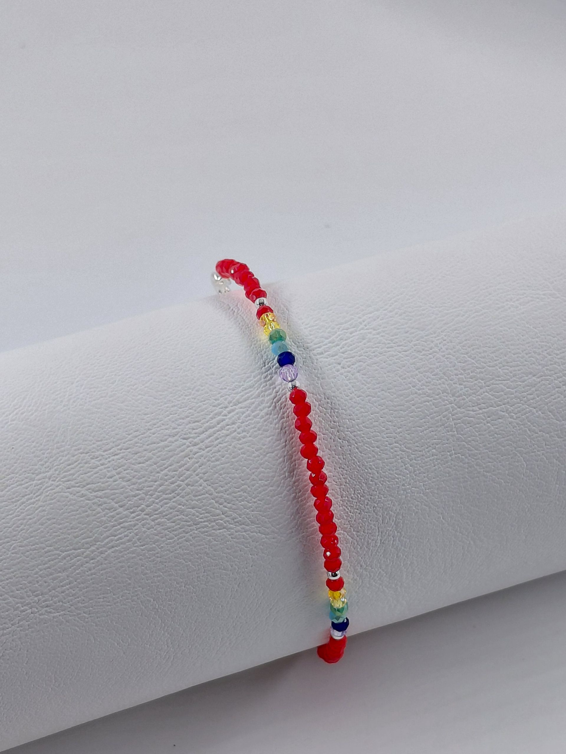 Pulsera de cuentas rojas con pequeñas cuentas azules, amarillas y verdes sobre un fondo blanco.