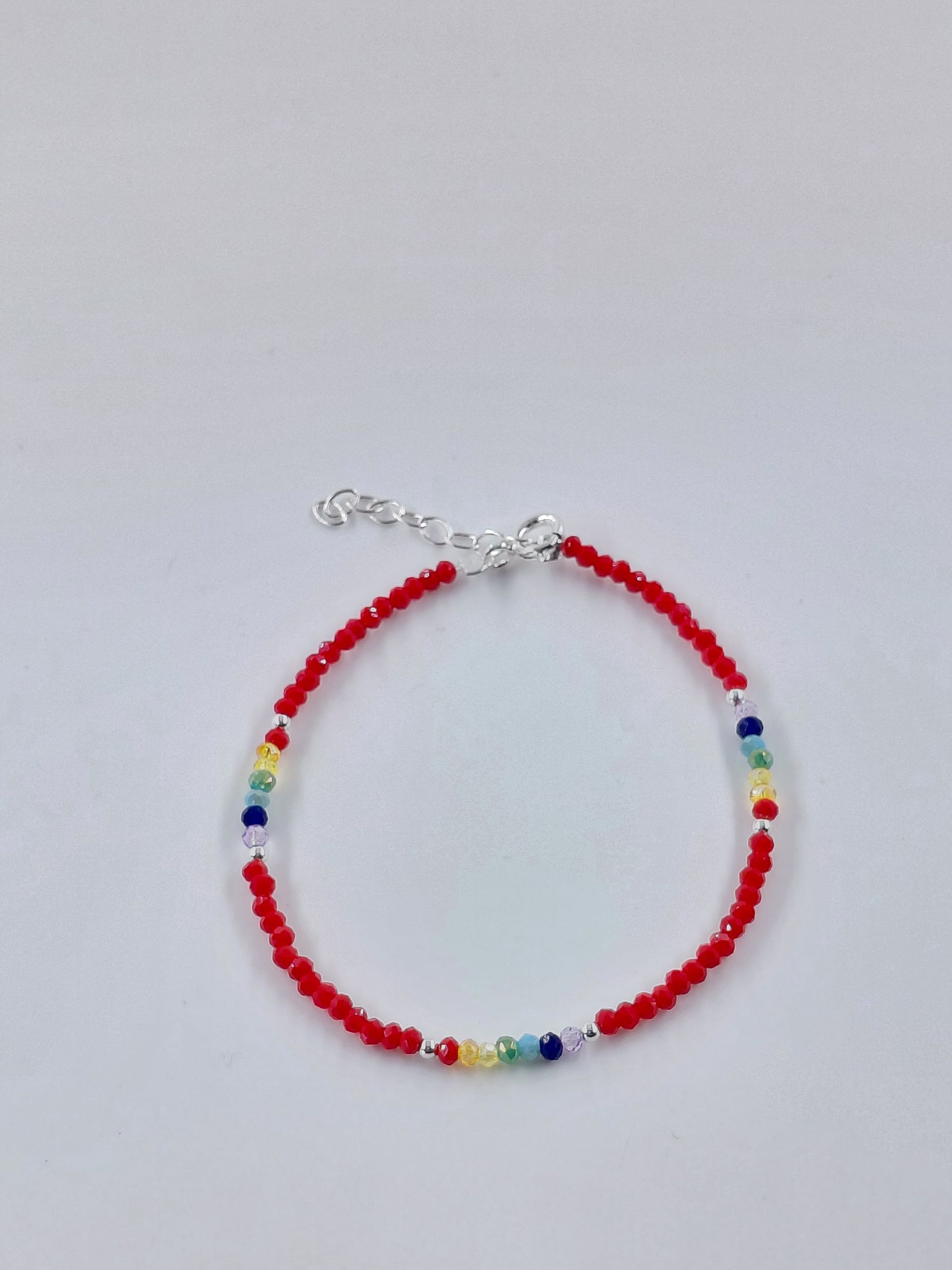 Pulsera de cuentas rojas con pequeñas cuentas azules, amarillas y verdes sobre un fondo blanco.