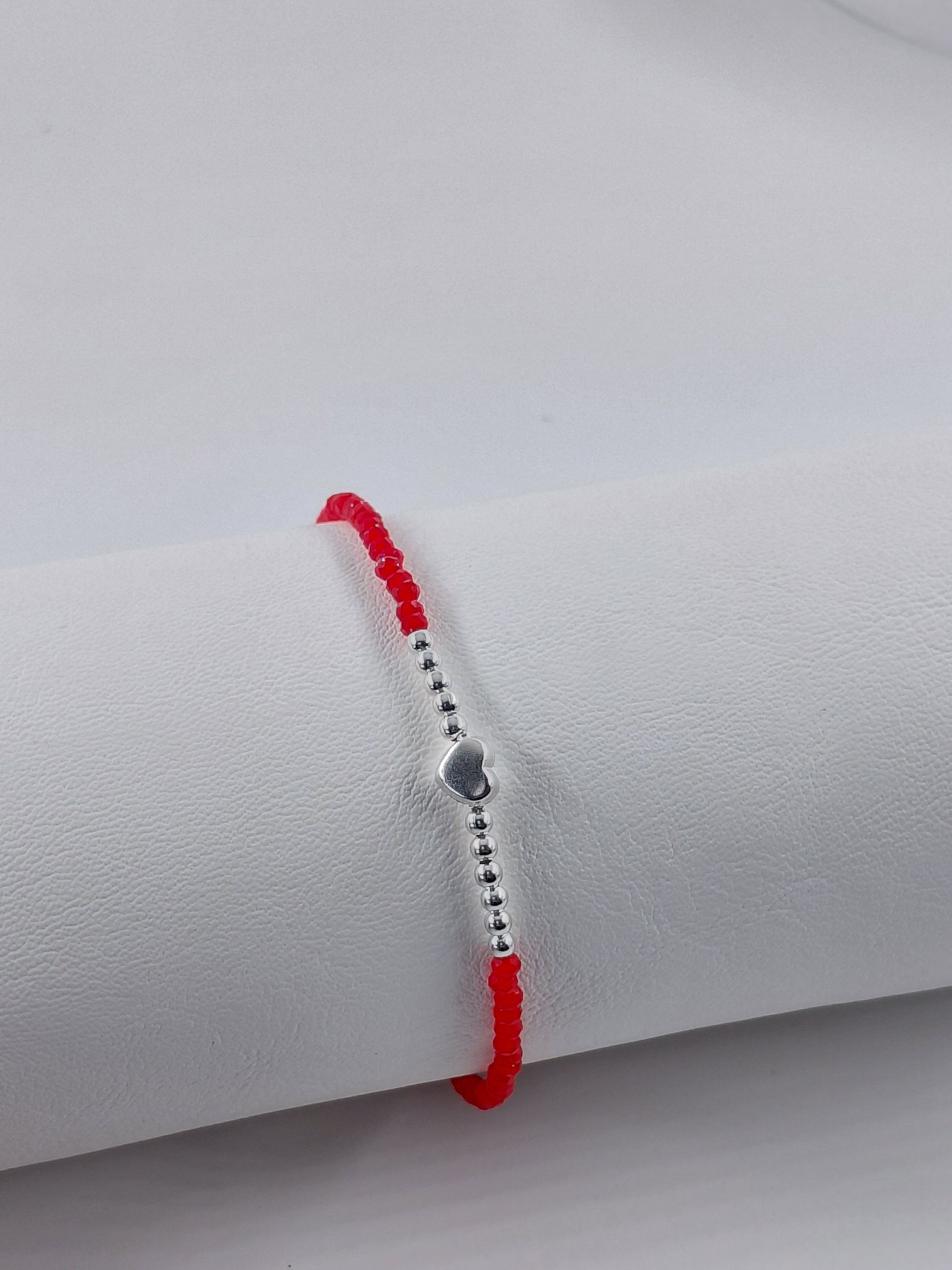 Pulsera de cuentas rojas con cierre plateado y dije de corazón sobre fondo claro.