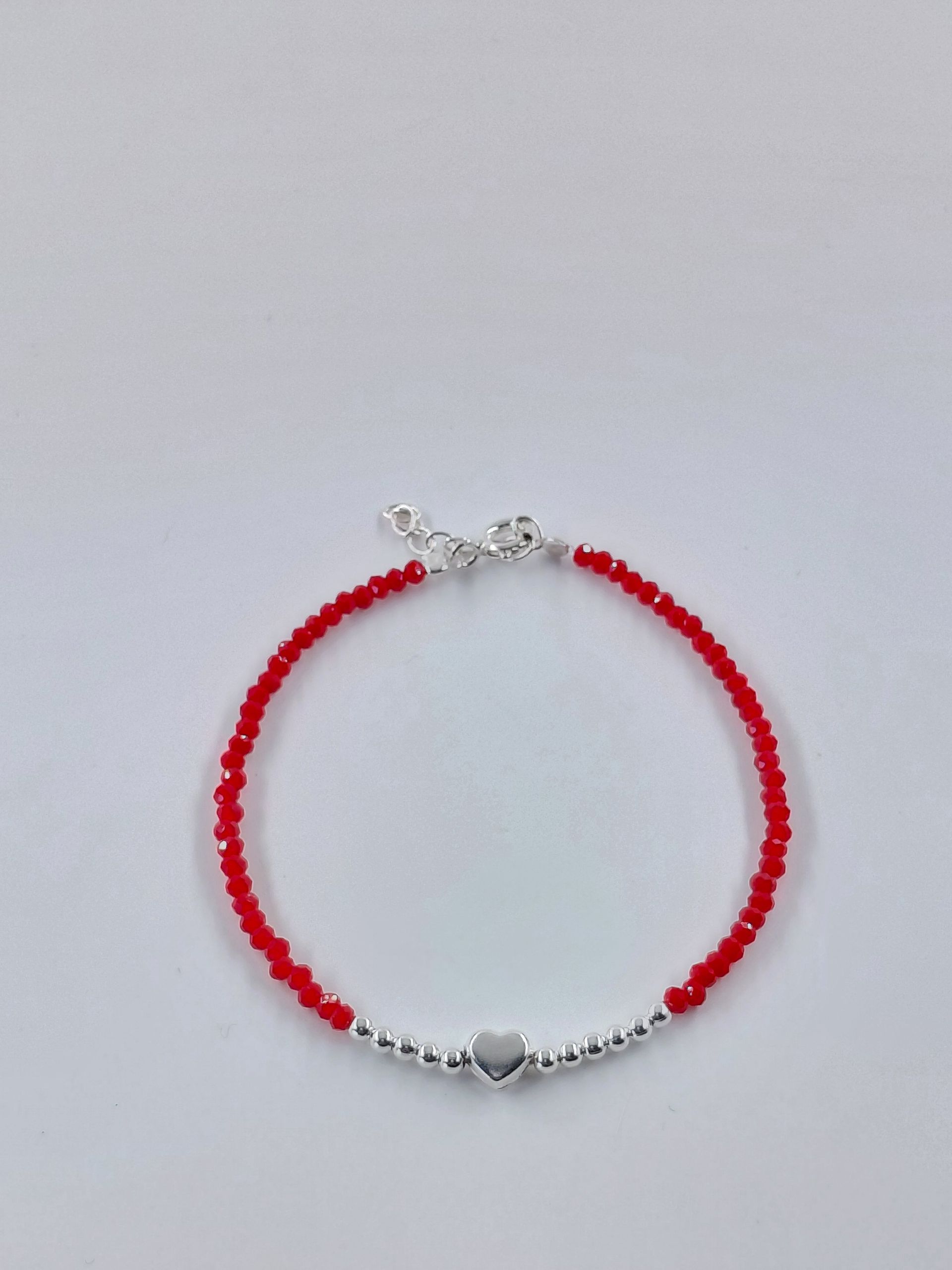 Pulsera de cuentas rojas con cierre plateado y dije de corazón sobre fondo claro.