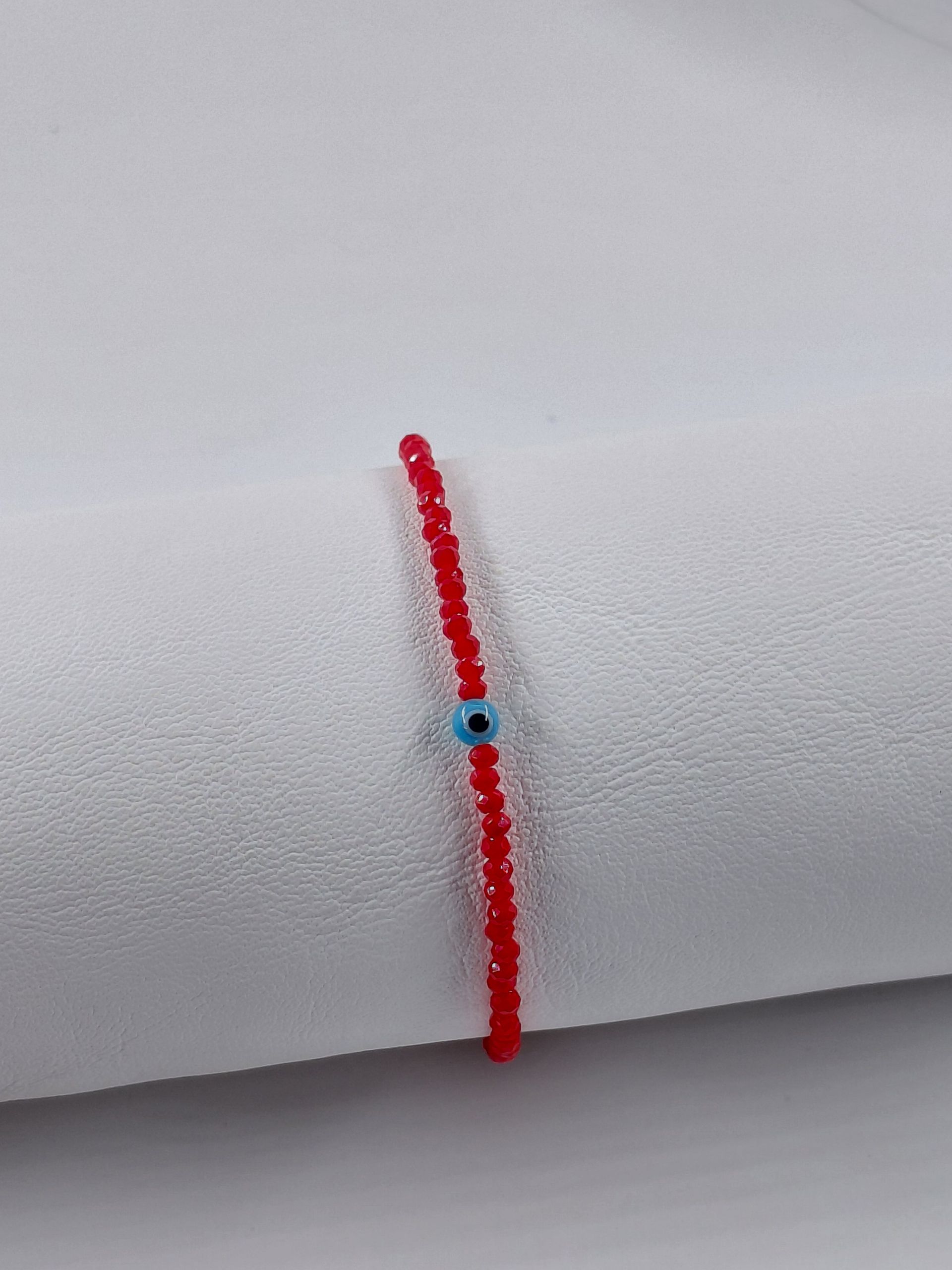 Pulsera de cuentas rojas con una pequeña cuenta azul y cierre plateado sobre fondo blanco.