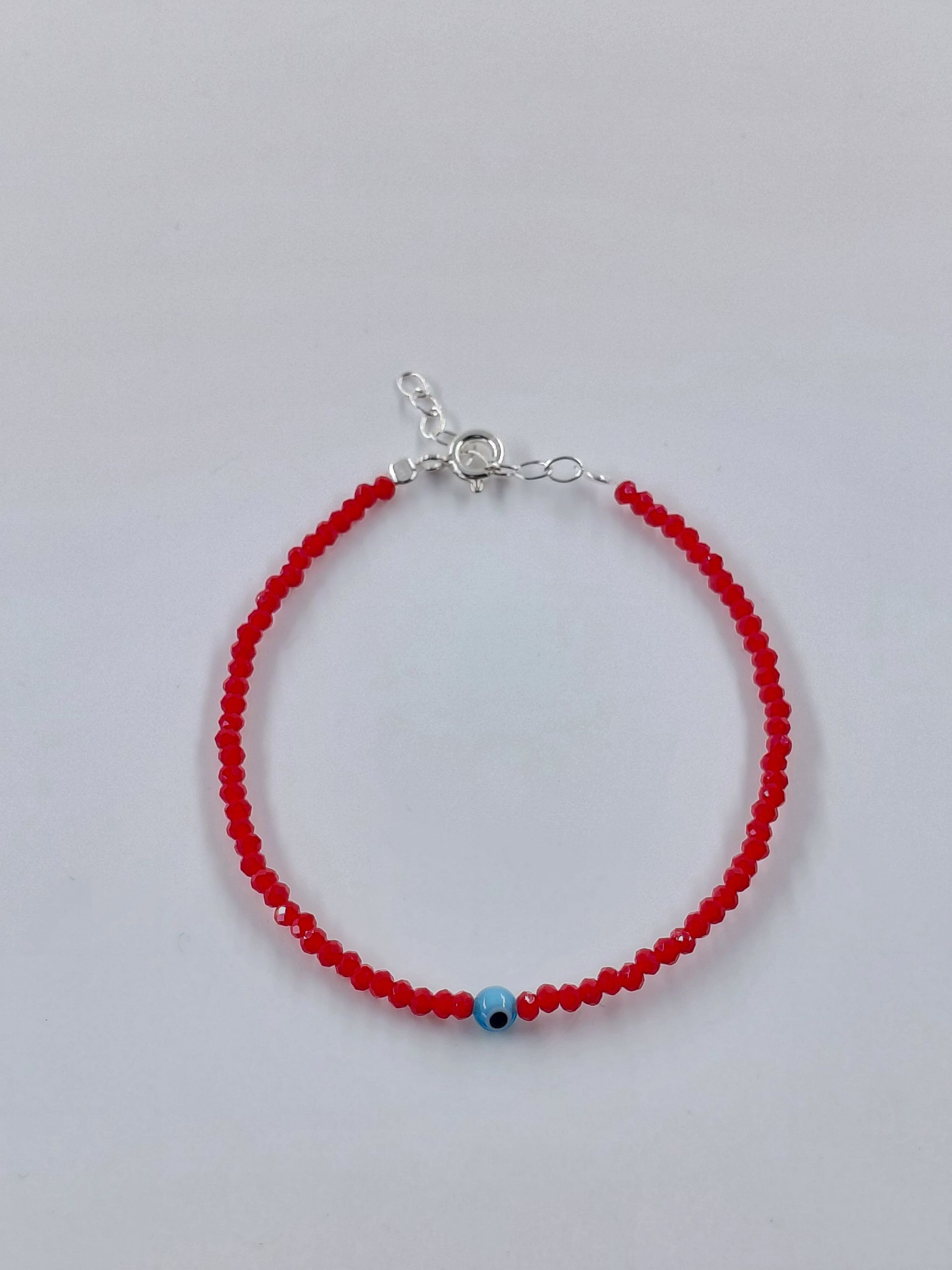 Pulsera de cuentas rojas con una pequeña cuenta azul y cierre plateado sobre fondo blanco.