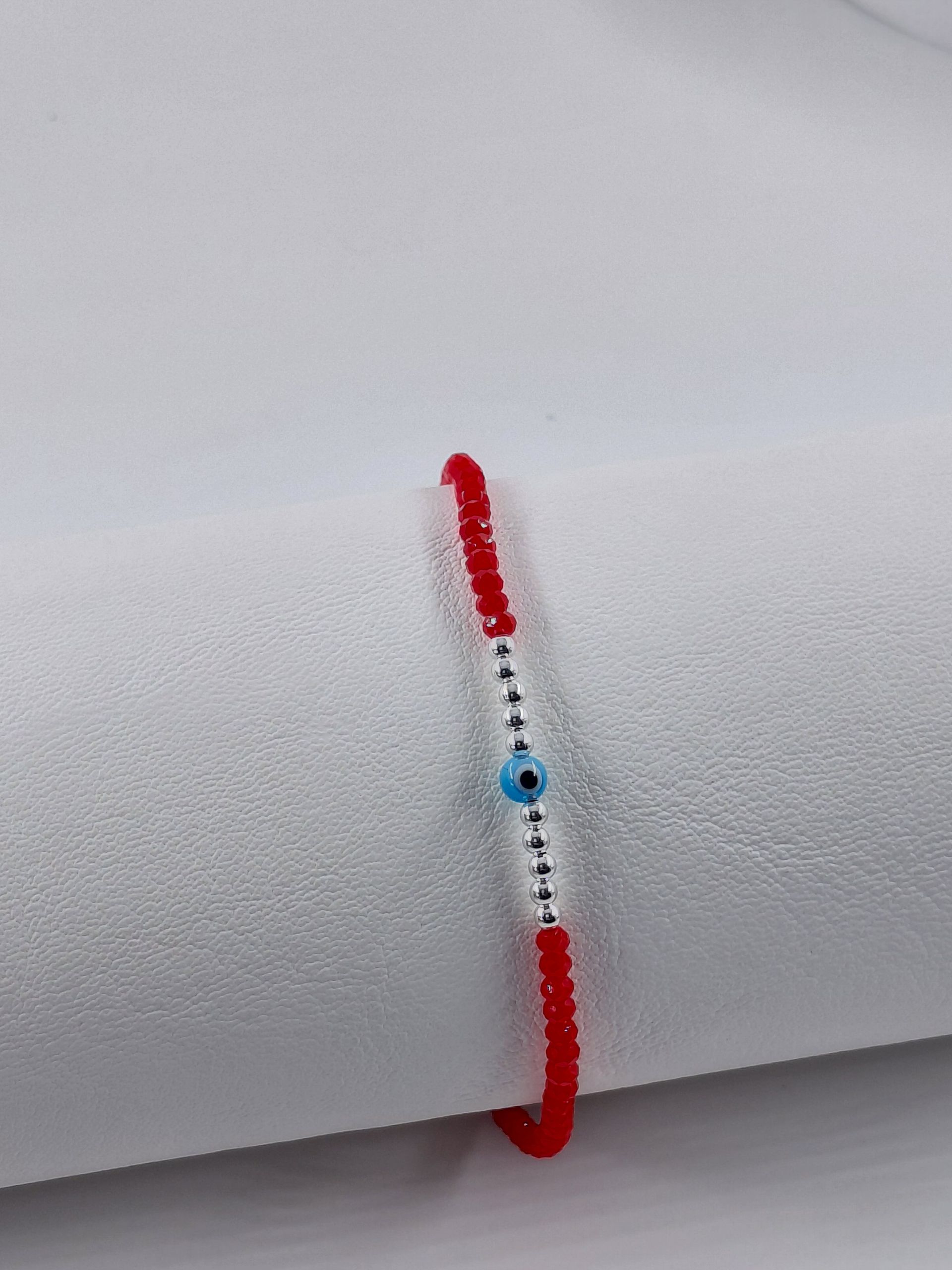 Pulsera de cuentas rojas con una cuenta azul y extremos de cordón ajustables sobre fondo blanco.