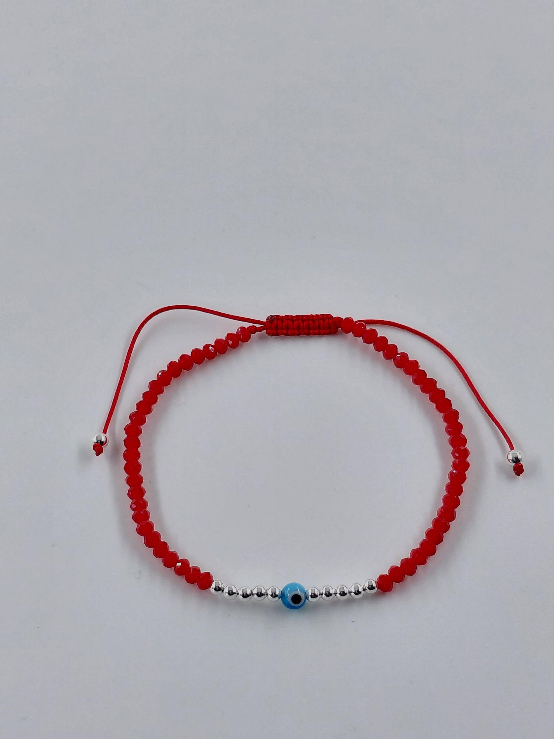 Pulsera de cuentas rojas con una cuenta azul y extremos de cordón ajustables sobre fondo blanco.
