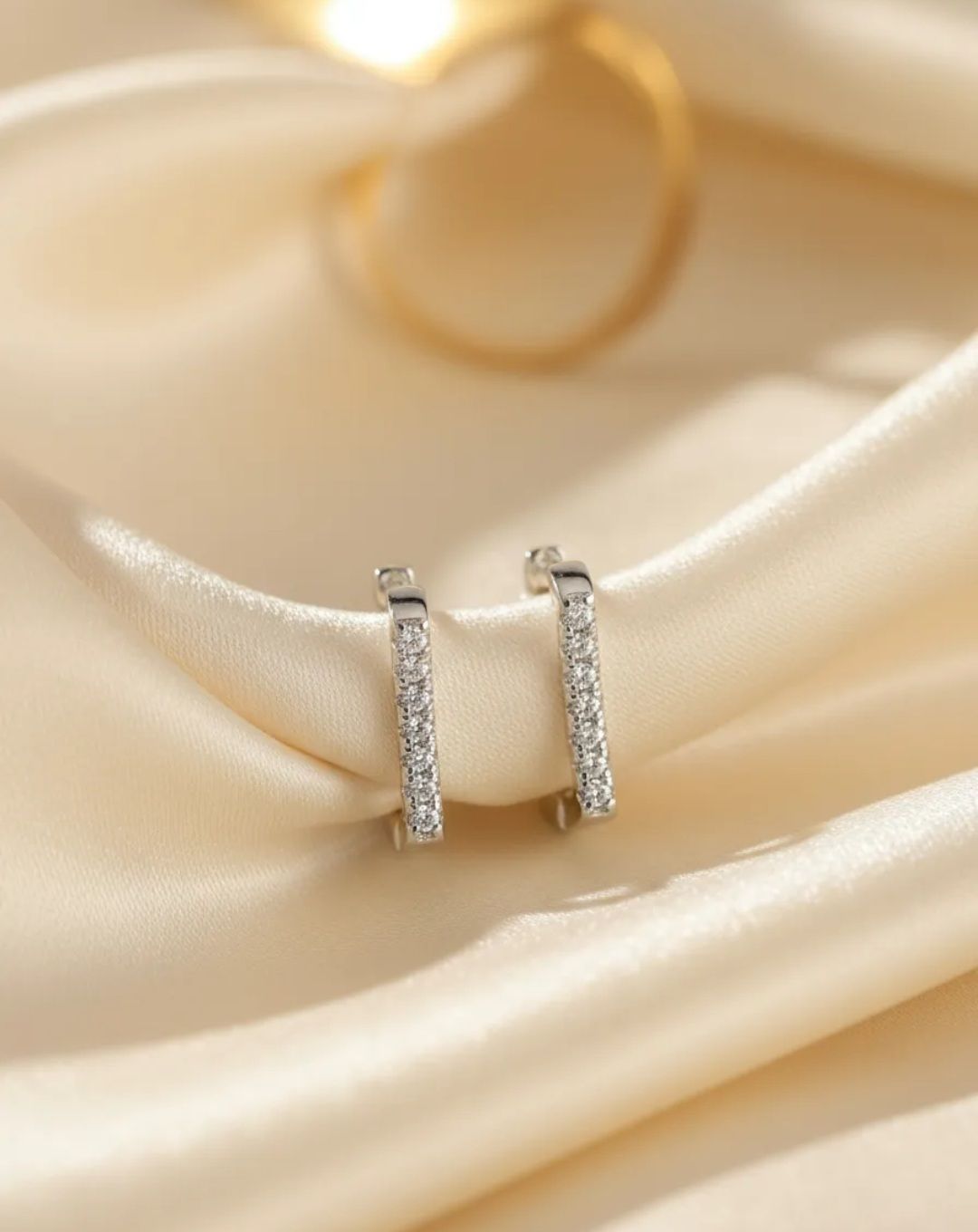 Dos pendientes rectangulares de plata con pequeños diamantes de imitación sobre una superficie de tela gris.