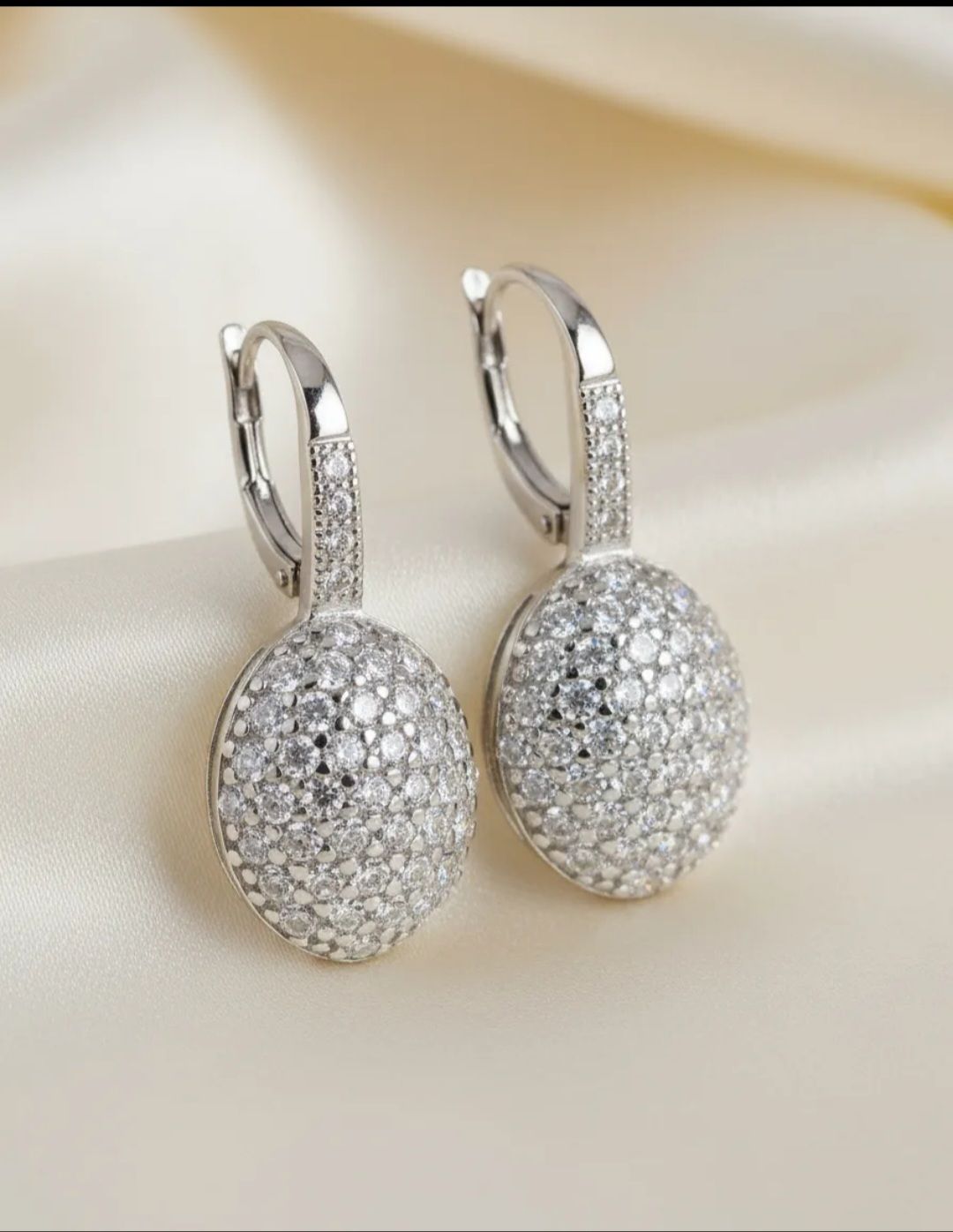 Par de pendientes colgantes de plata con engastes redondos tipo pavé que imitan diamantes sobre un fondo de mármol.