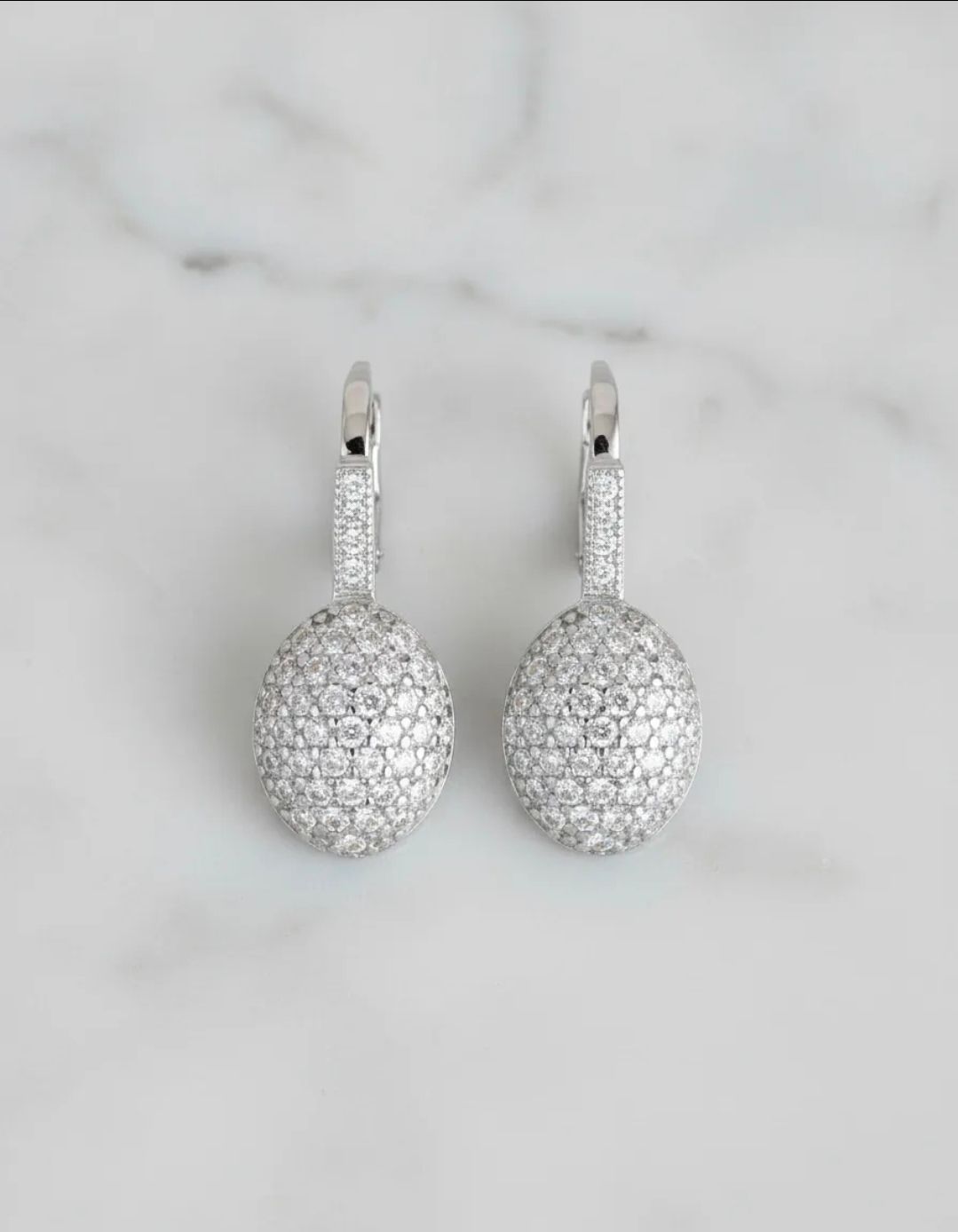 Par de pendientes colgantes de plata con engastes redondos tipo pavé que imitan diamantes sobre un fondo de mármol.