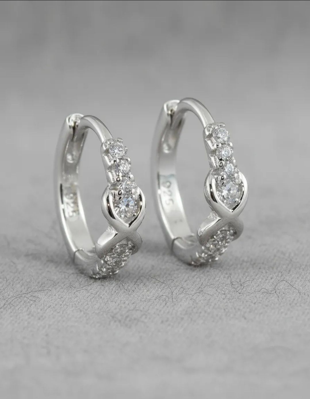 Pendientes de aro de plata con piedras preciosas transparentes agrupadas sobre un fondo gris.